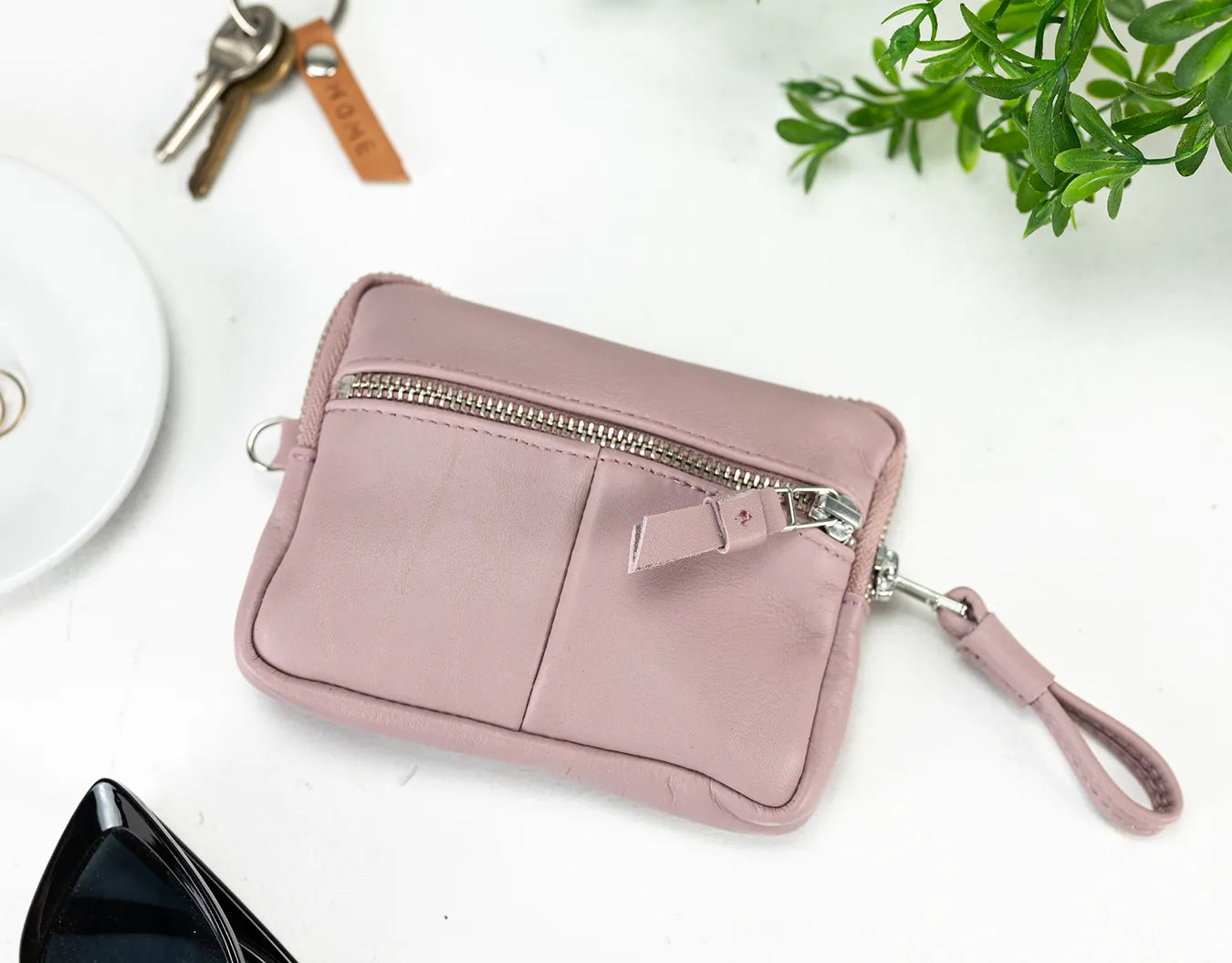 Pink wristlet with a keychain and plant on a white surface