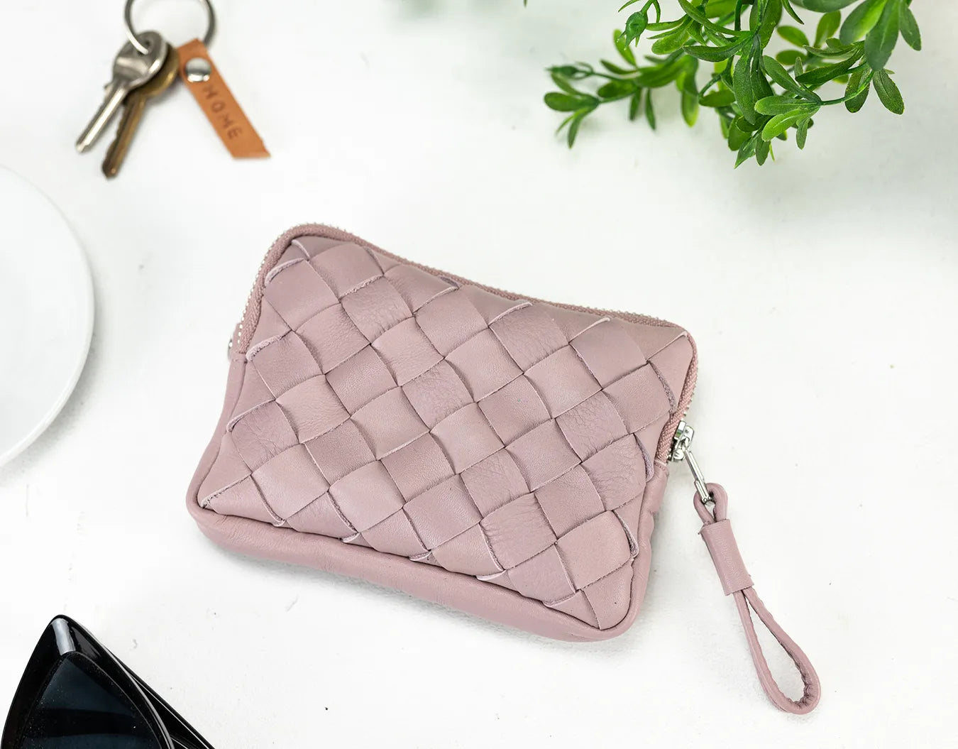 Pink woven pouch with a keychain on a white surface with a plant in the background
