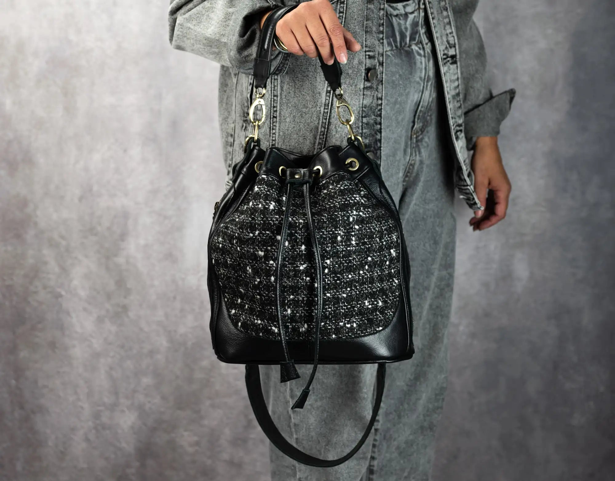 Person holding a black textured handbag against a gray background