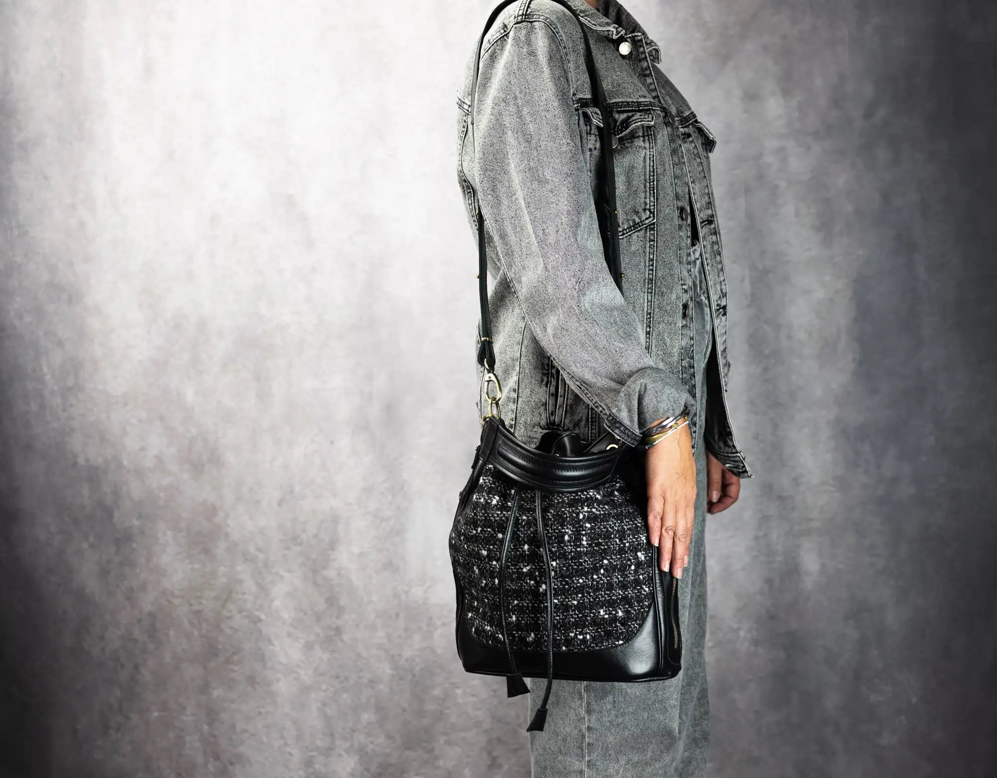 Person wearing a denim jacket and holding a black textured bag against a gray background