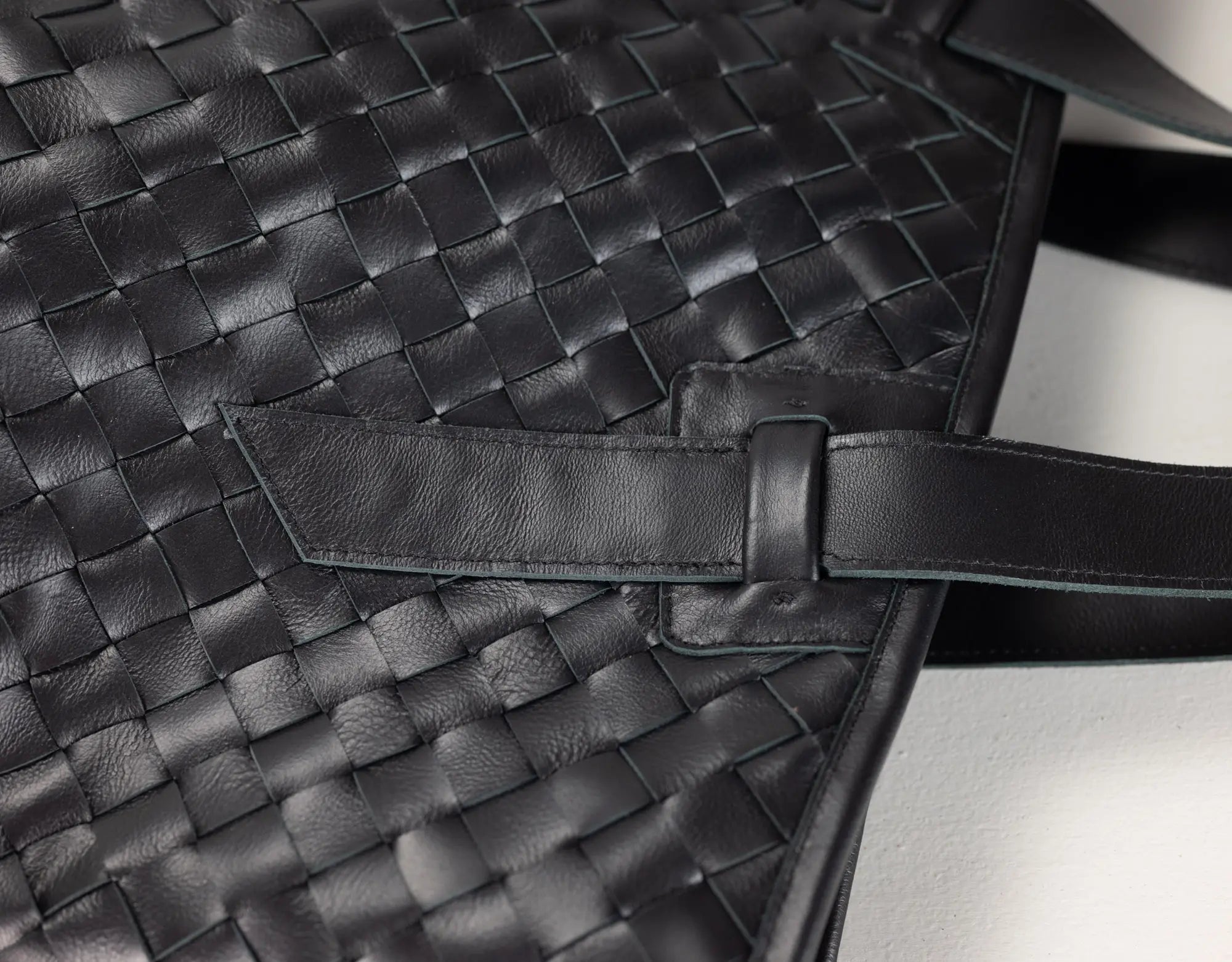 Close-up of a black woven leather bag with a strap detail and textured leather surface.