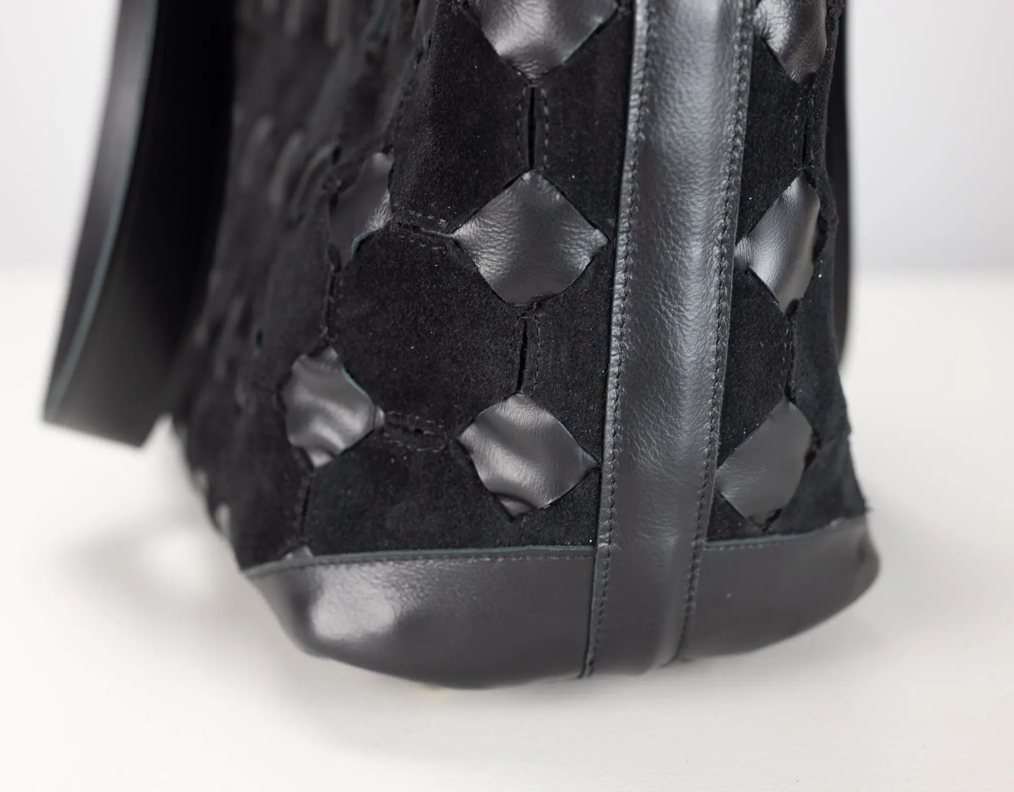 Close-up of a black woven leather handbag showing the textured geometric pattern and dark sole on a white background.