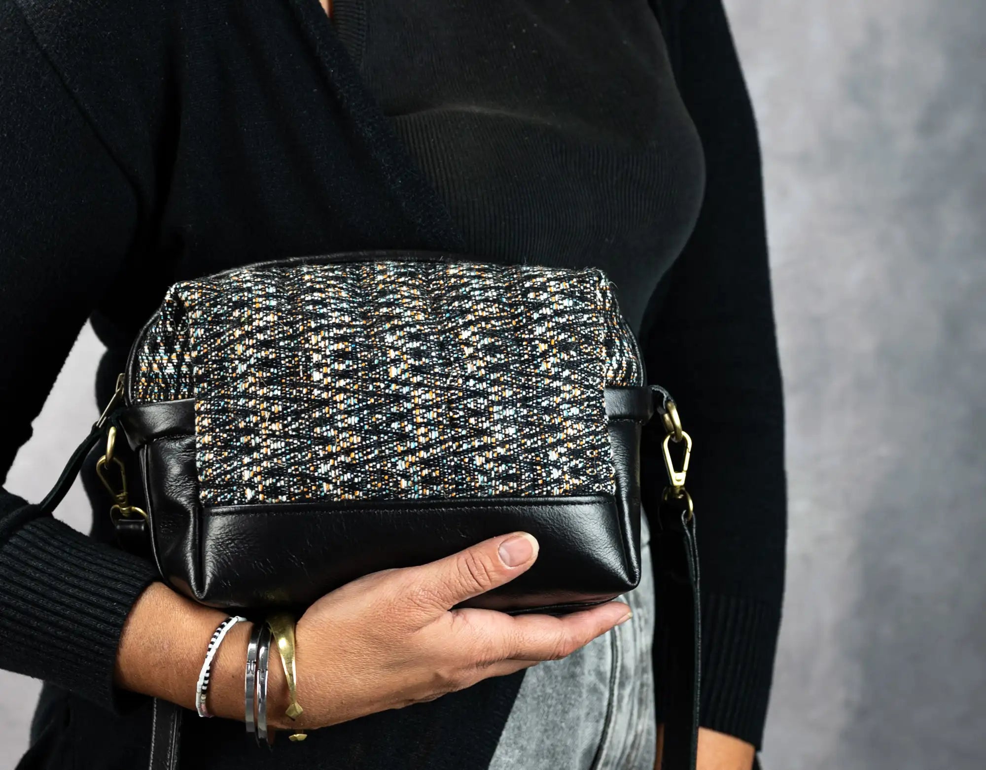 Person holding a black and silver patterned handbag against a gray background