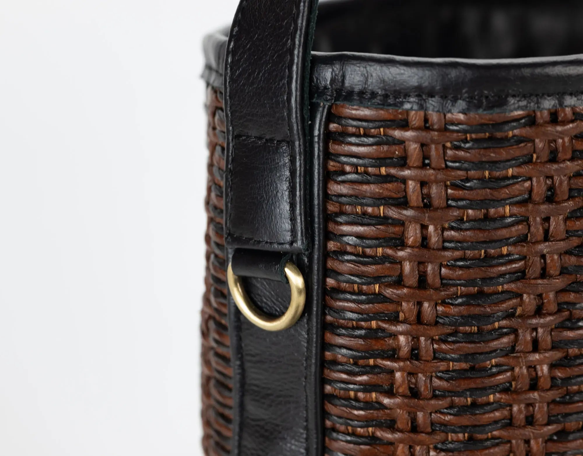 Close-up of a brown woven handbag with black leather strap and gold clasp on a white background