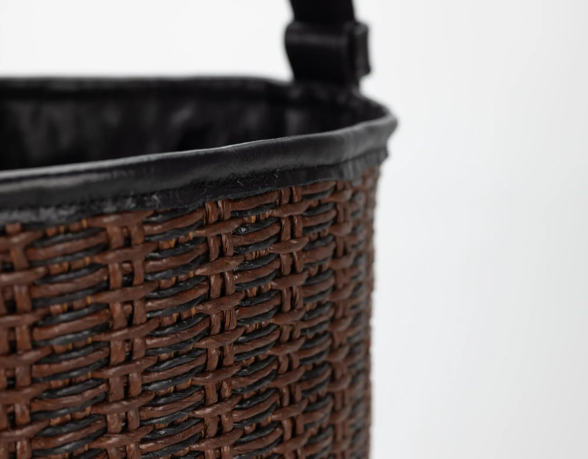 Close-up of a woven brown basket with a black handle on a white background