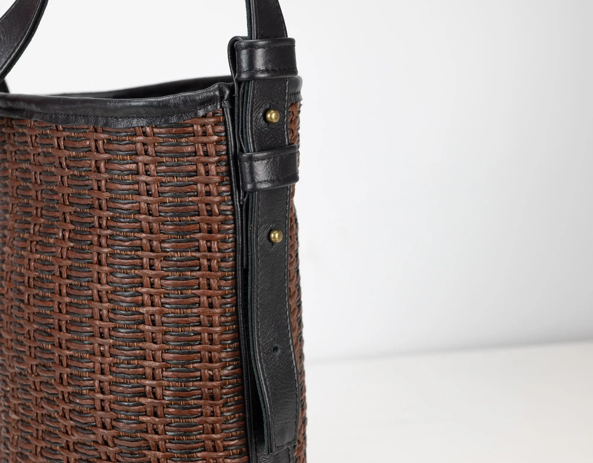 Brown woven handbag with black strap on a white background