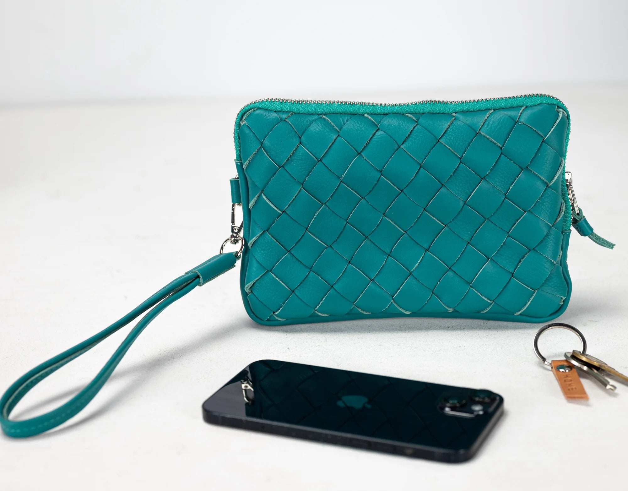 Teal woven clutch bag with a phone and keys on a white background