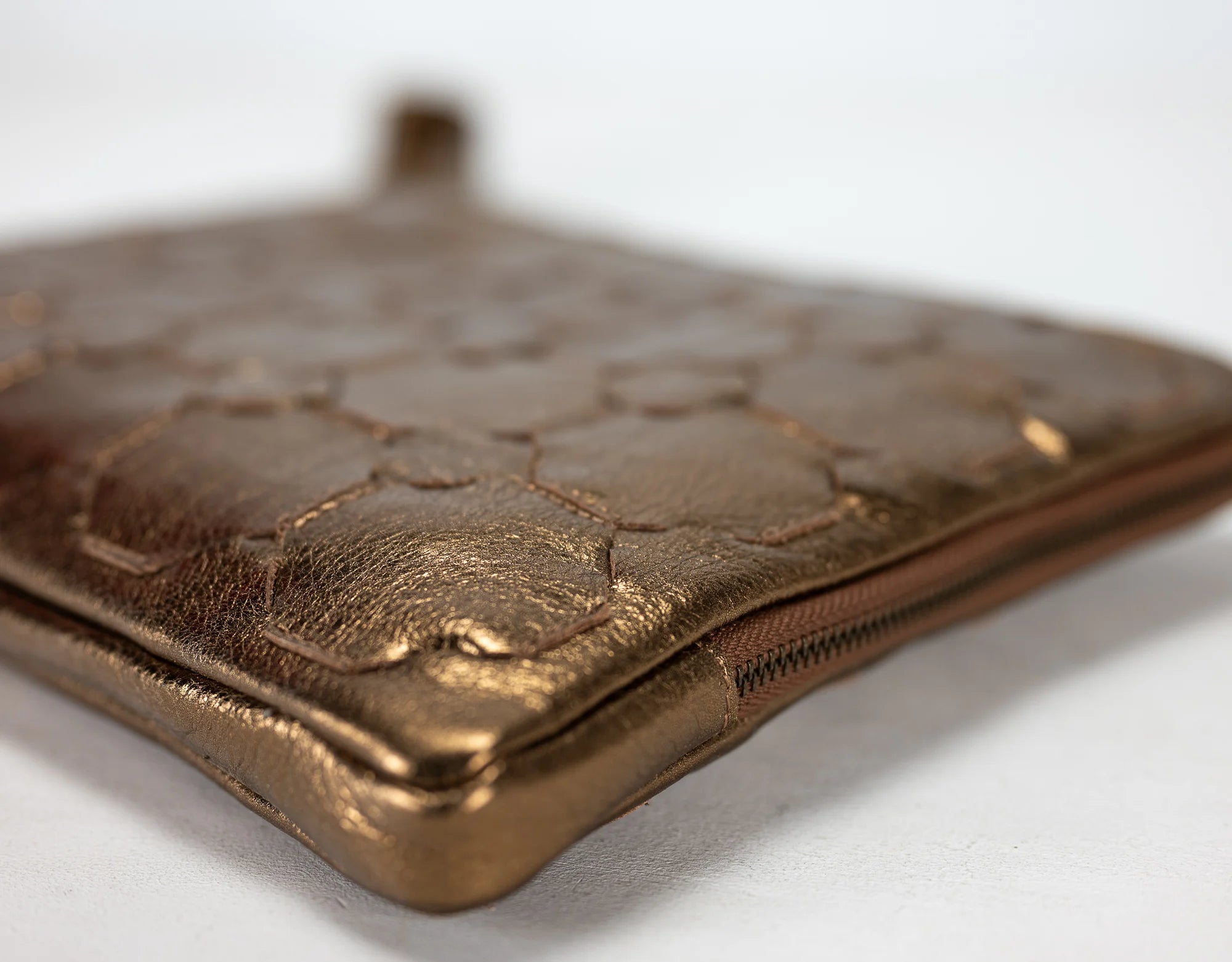 Bronze-colored clutch bag with embossed design on a white background