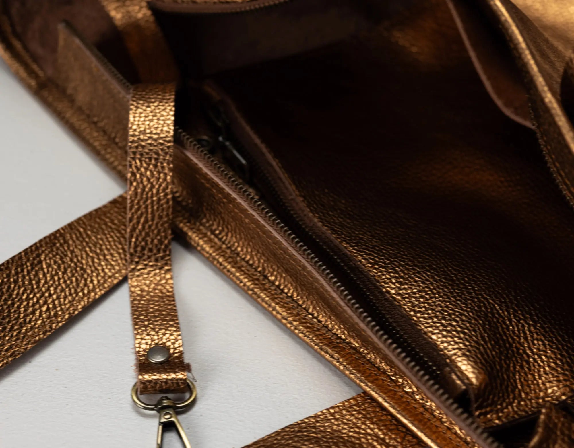 Close-up of a metallic bronze textured leather bag showing the interior zip pocket and strap attachment.