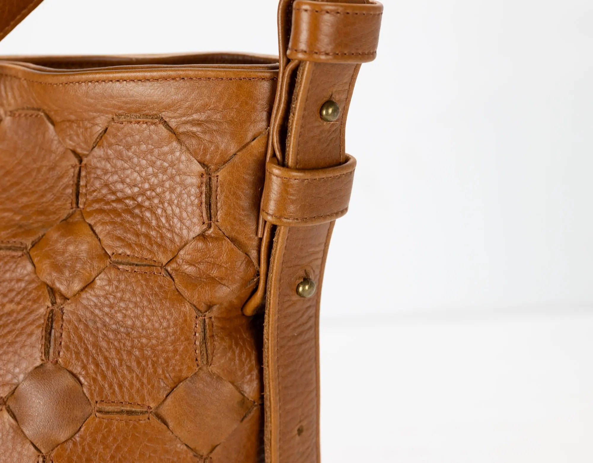 Close-up of a brown leather handbag with textured surface and visible stitching on a white background.