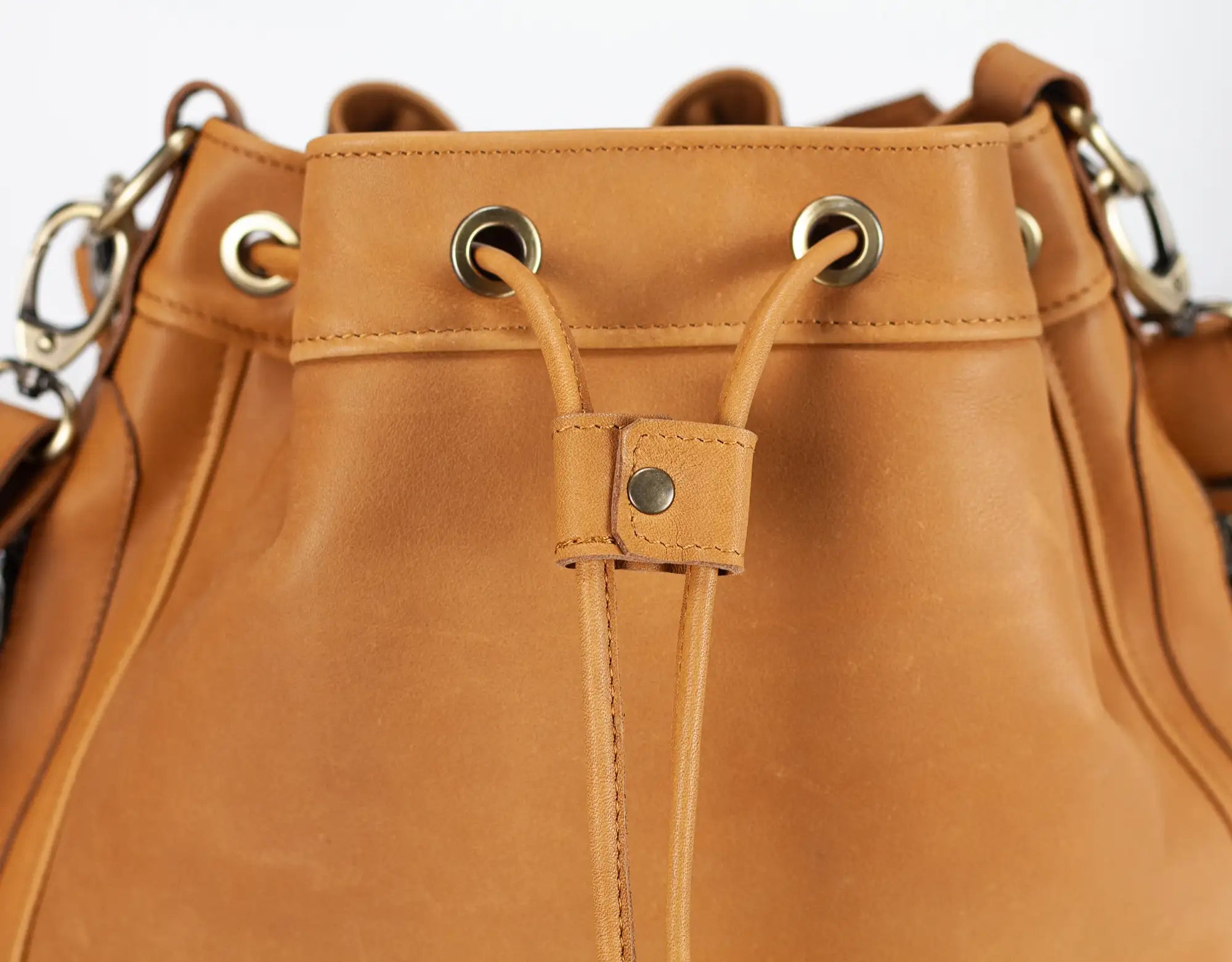 Close-up of a brown leather bucket bag with metal eyelets and straps.