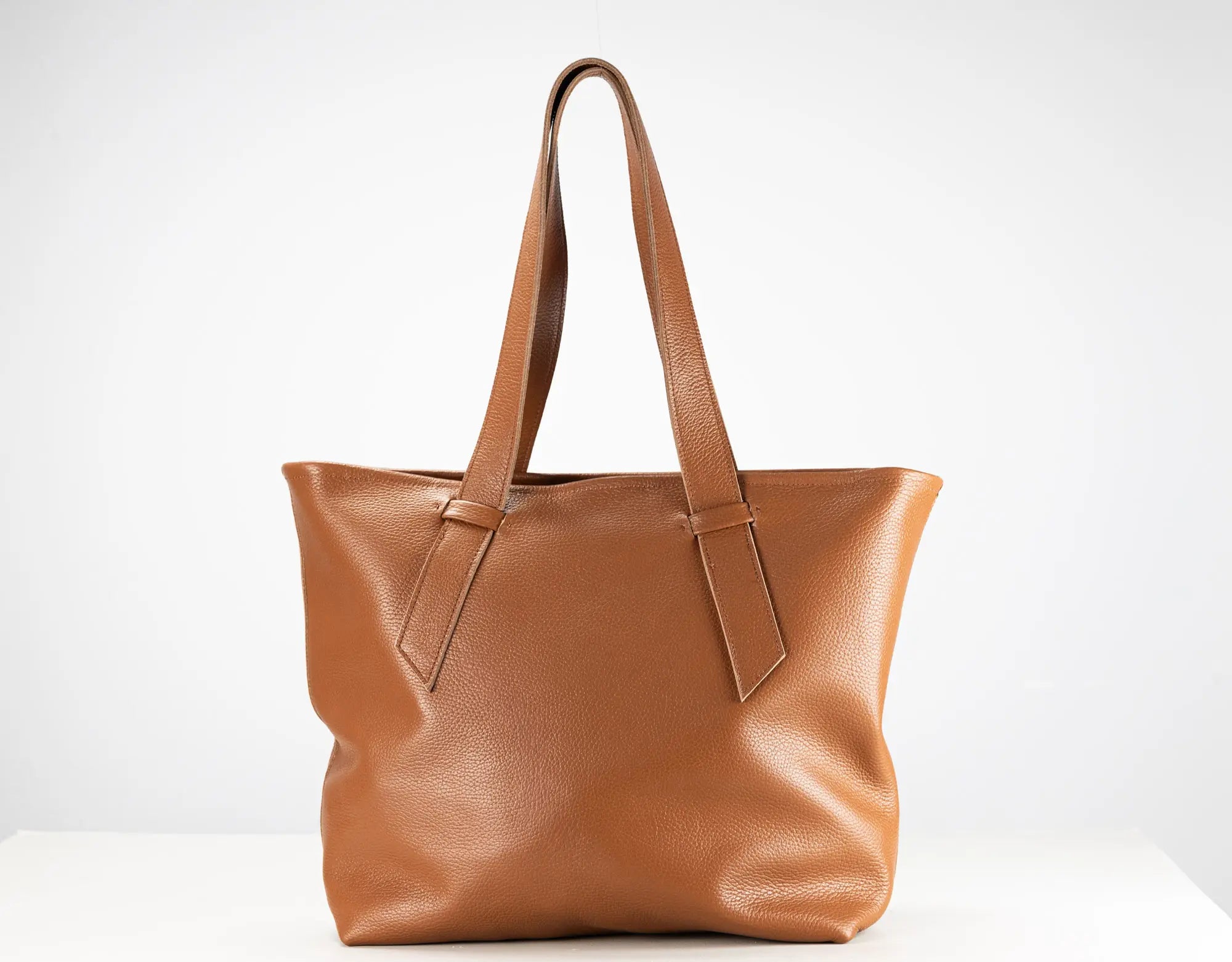 A medium brown leather tote bag with dual shoulder straps, displayed against a clean white background.