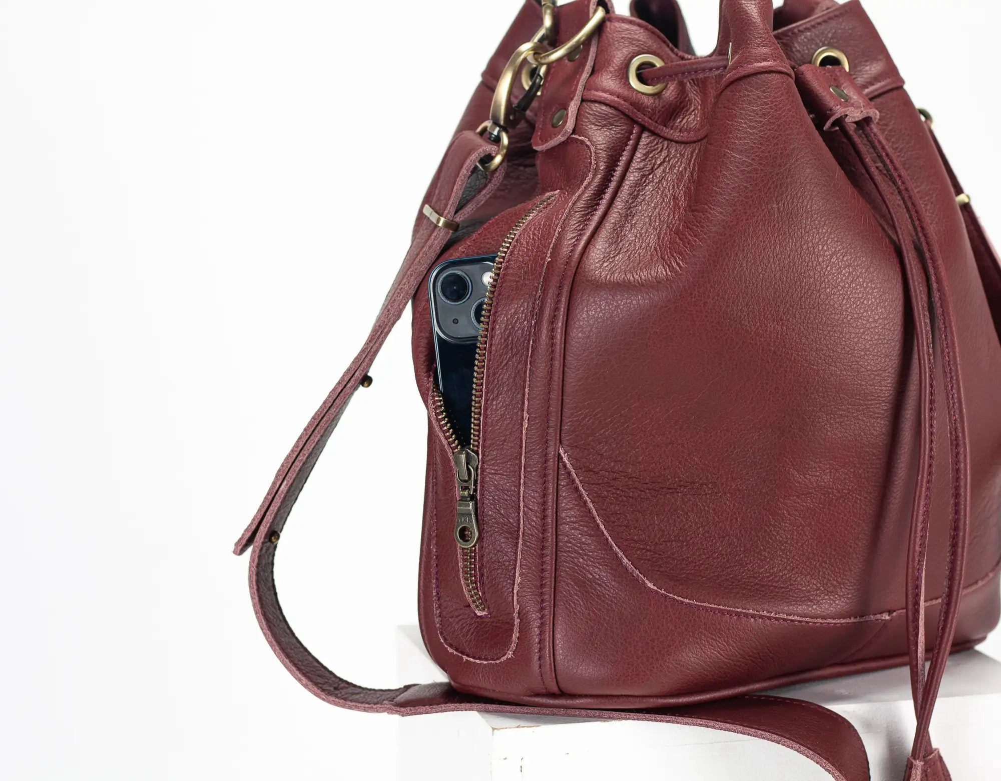 Burgundy leather handbag with a visible zipper pocket on a white background
