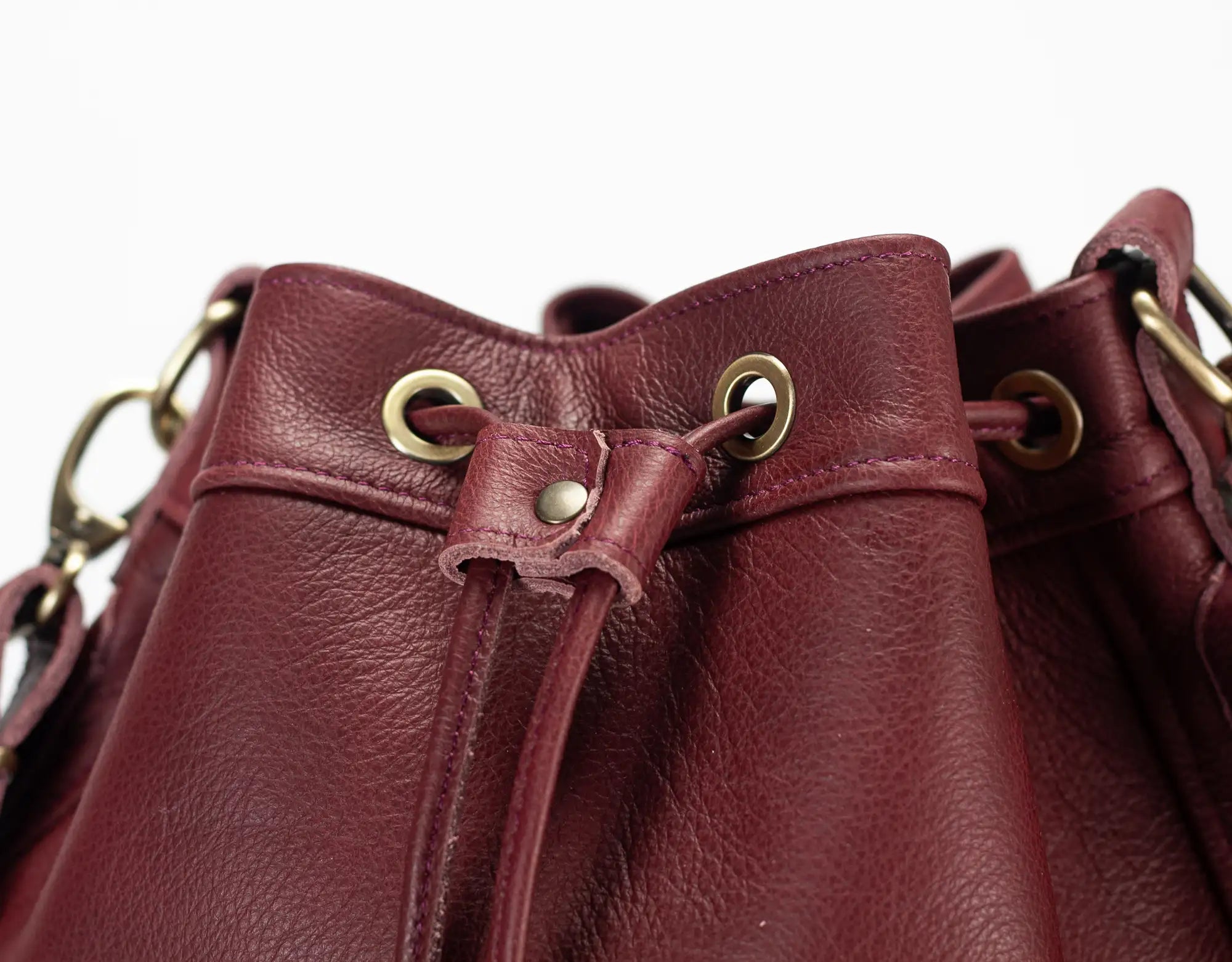 Close-up of a maroon leather drawstring bag with brass eyelets on a white background