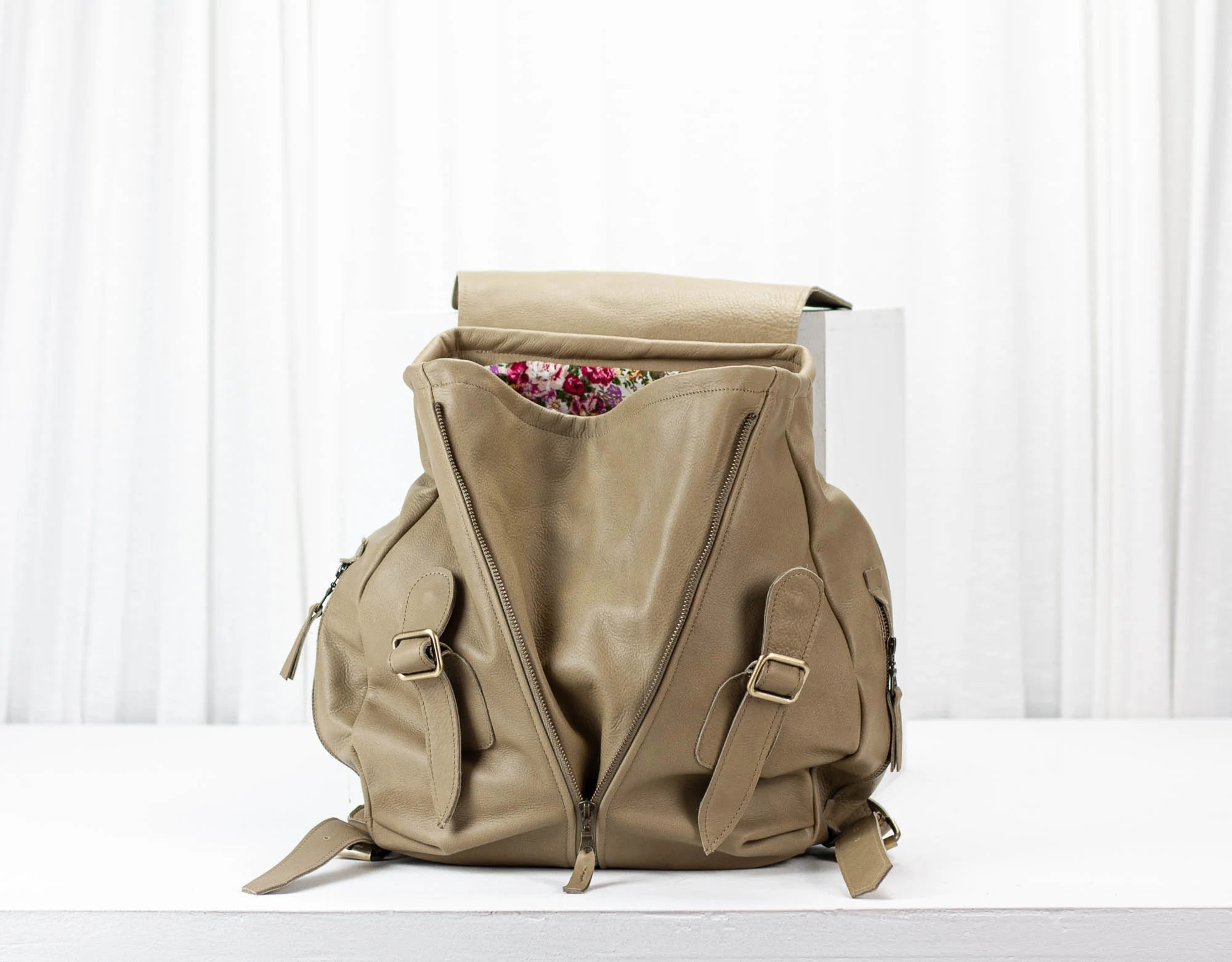 Beige backpack with floral items peeking out on a white background
