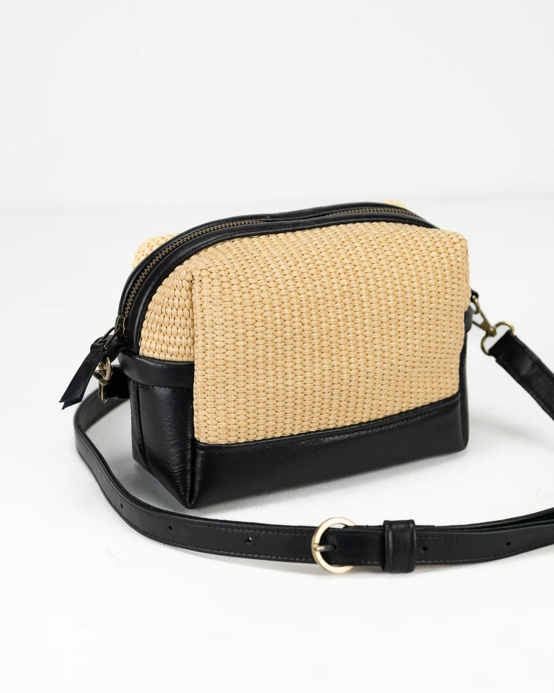 Crossbody bag with straw-like texture and black leather accents on a white background