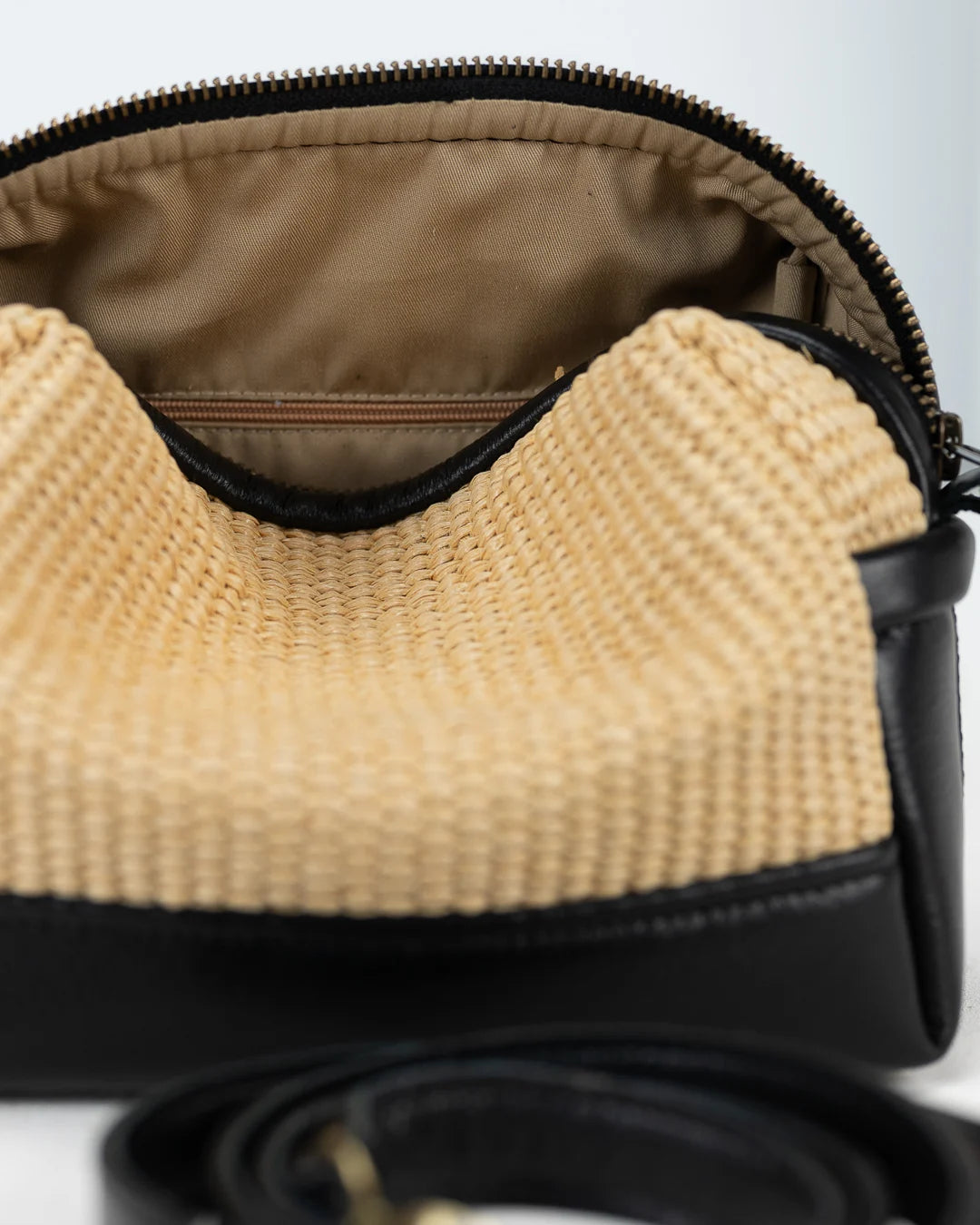 Close-up of a straw handbag with a black strap on a white background