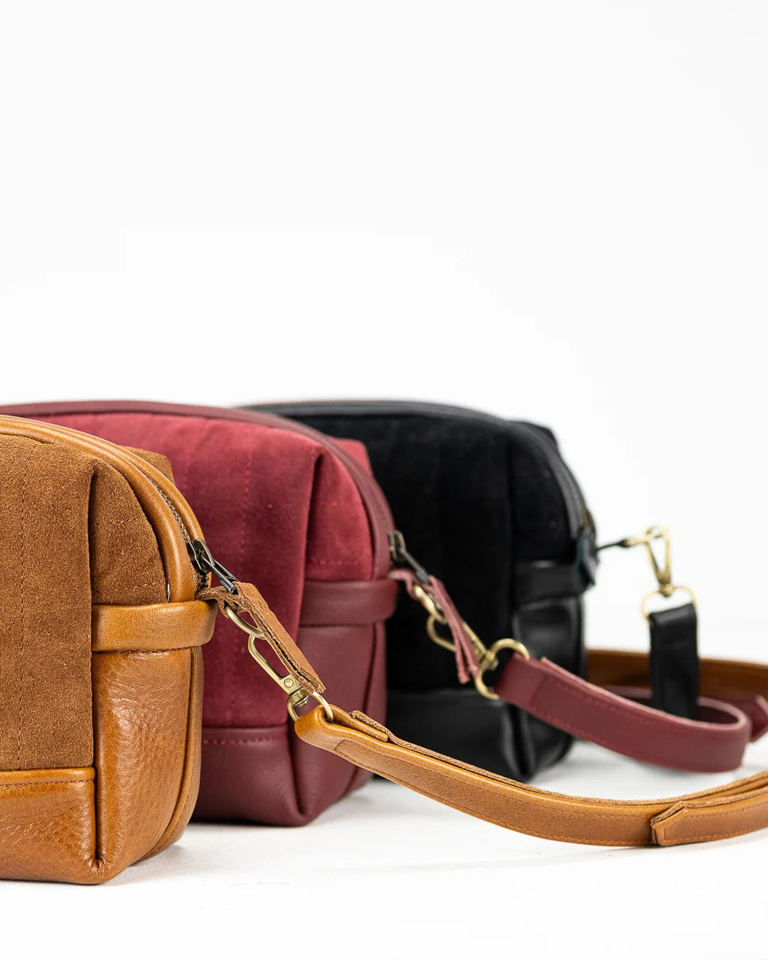 Three leather bags in brown, red, and black on a white background