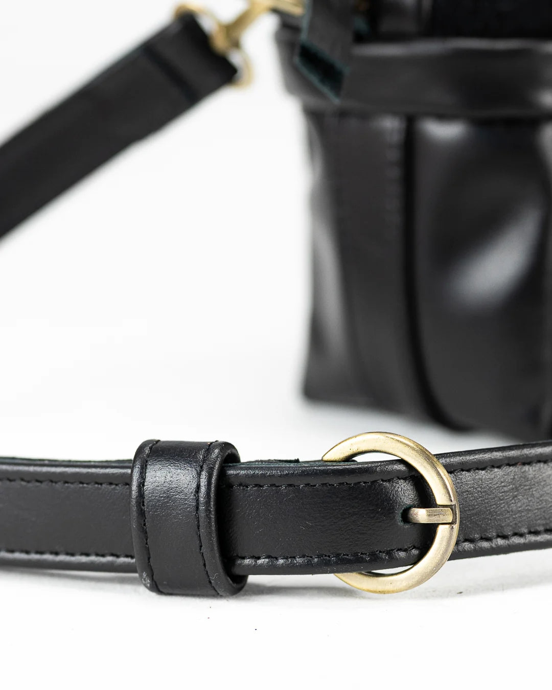 Close-up of a black leather belt with a gold buckle on a white background
