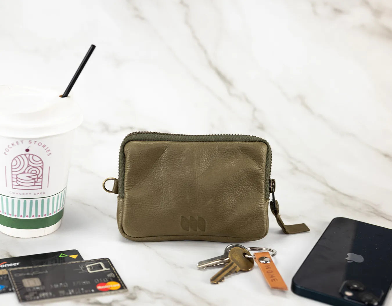 Green pouch with keys, phone, and cards on a white surface