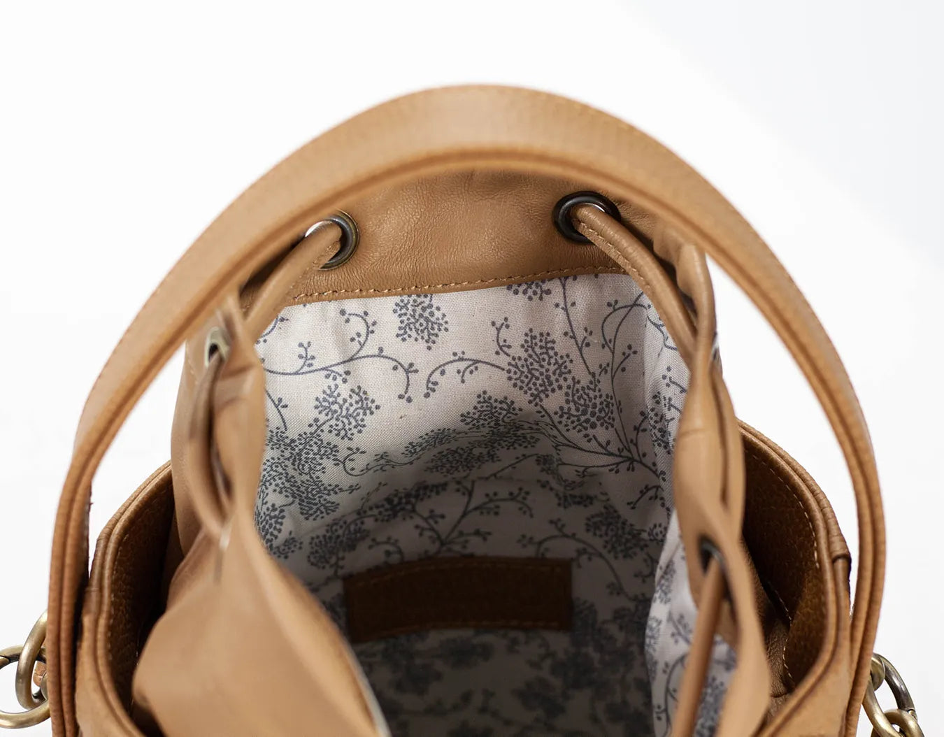 Close-up of a tan leather handbag with floral lining on a white background