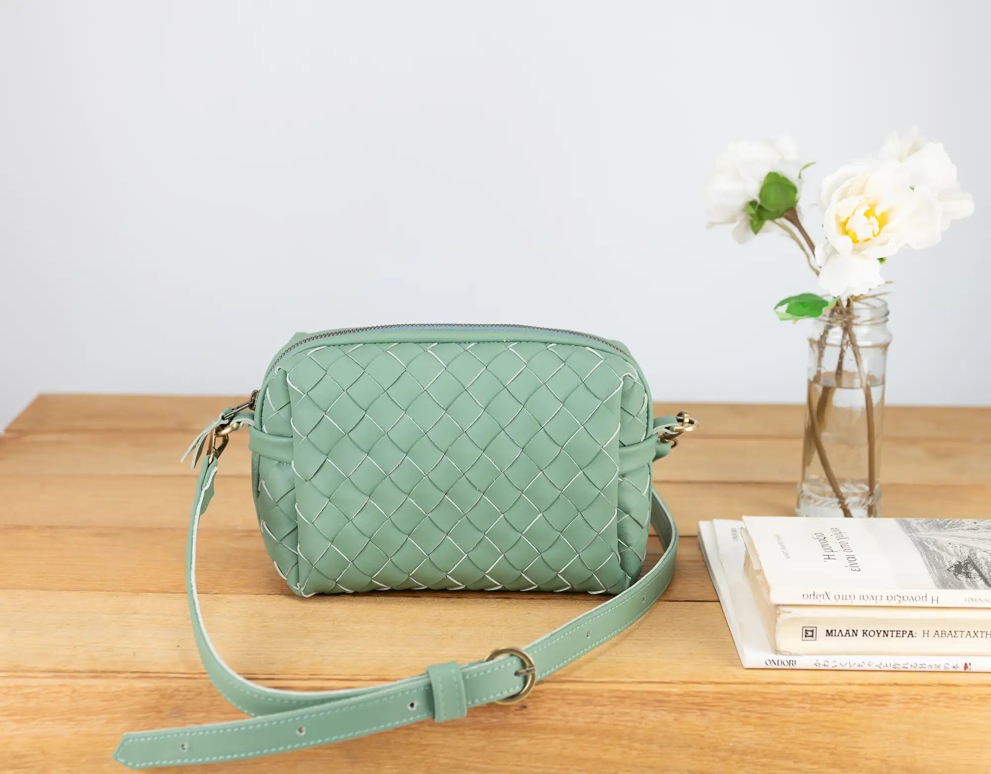 Green woven handbag on a wooden surface with a white background