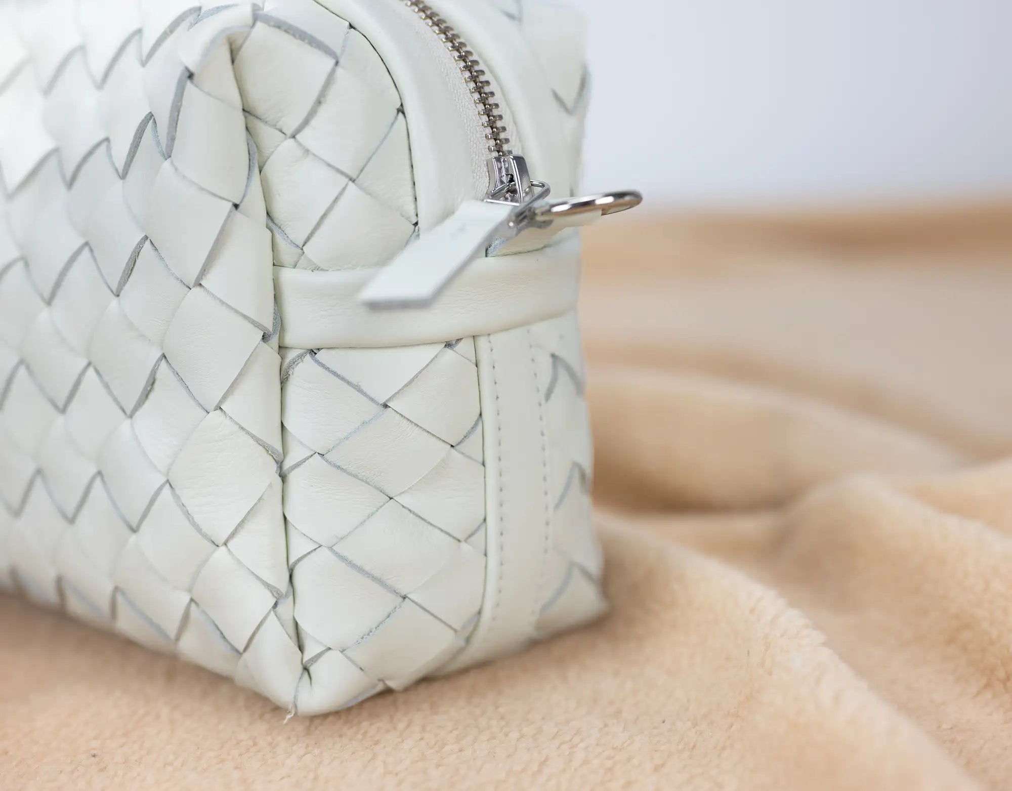 White woven handbag on a beige surface with a blurred background