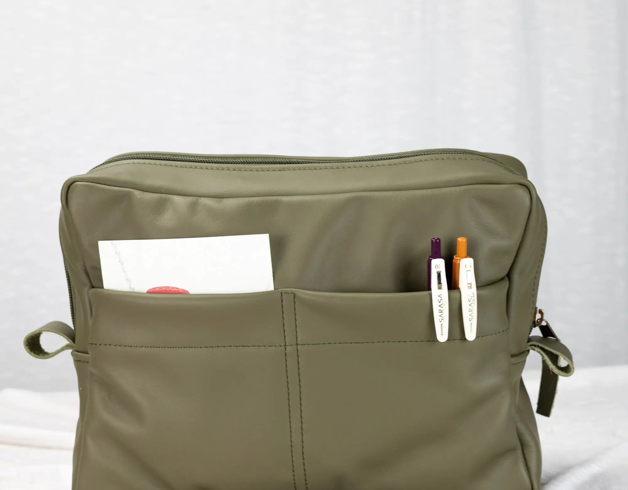 Green bag with pockets containing stationery items on a white background