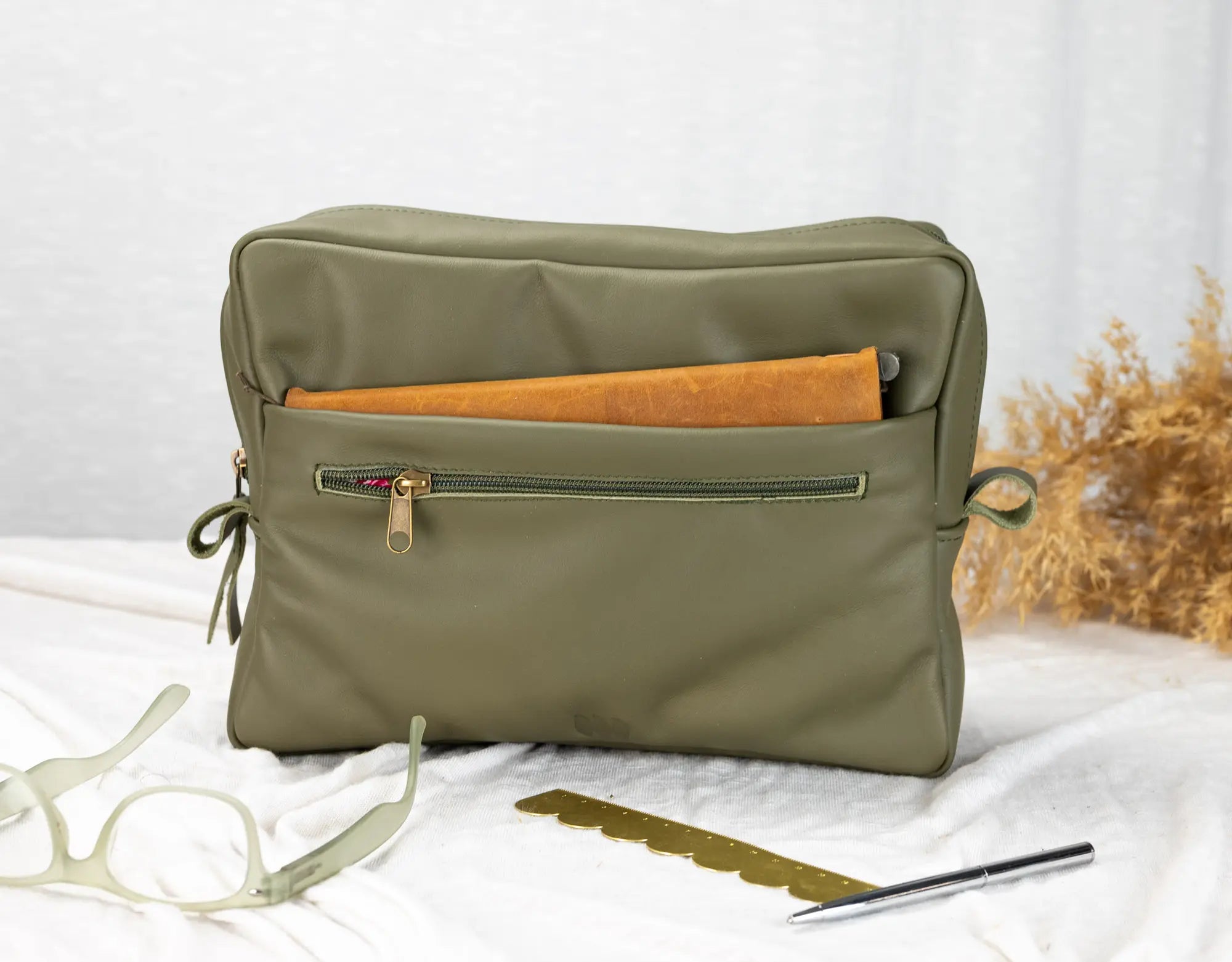Green toiletry bag with a zipper on a white surface with a blurred natural background
