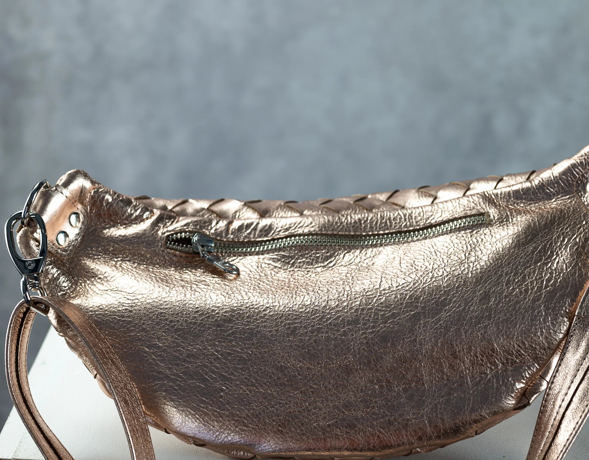 Metallic rose gold handbag with braided detail on a gray background