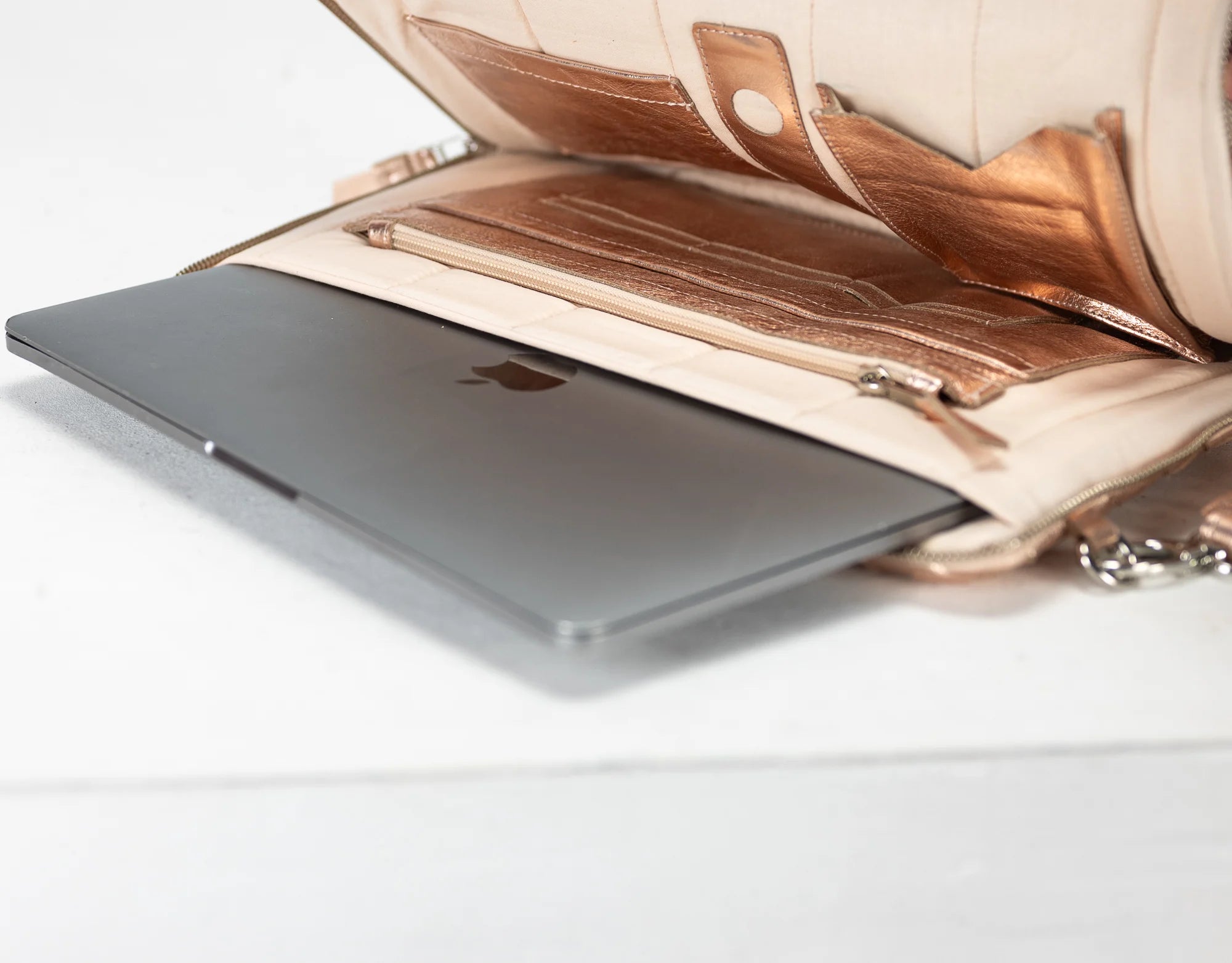 Silver laptop with Apple logo inside an open beige handbag on a white background