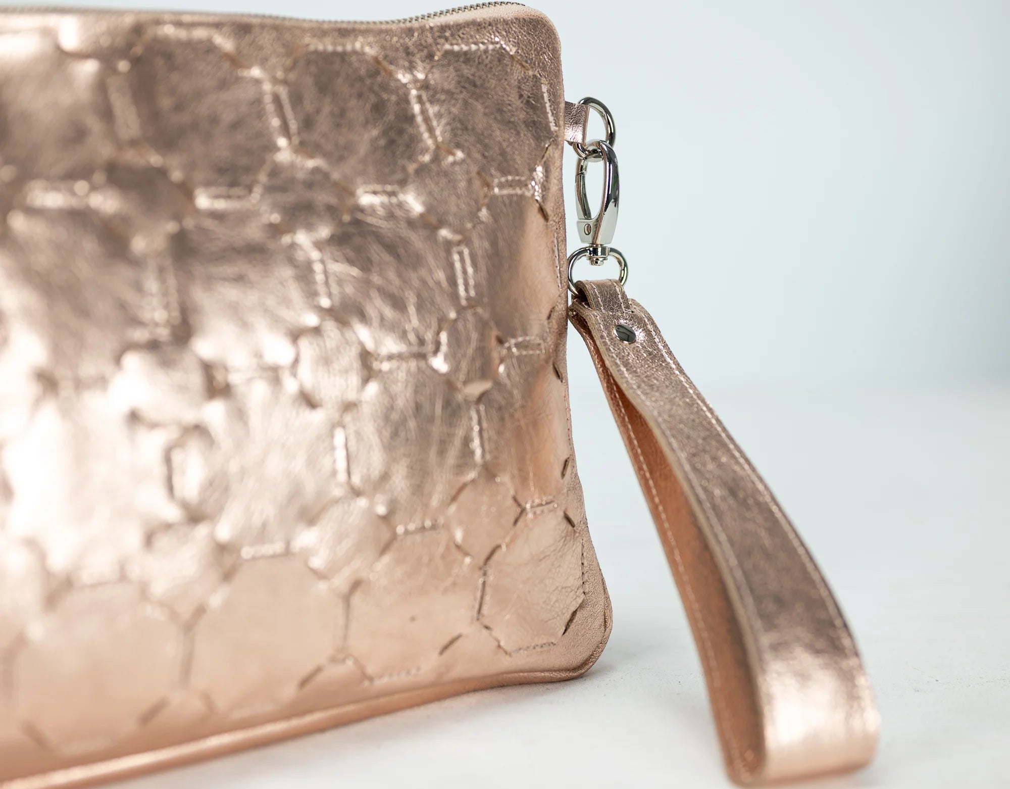 Rose gold textured clutch bag with a strap on a light background