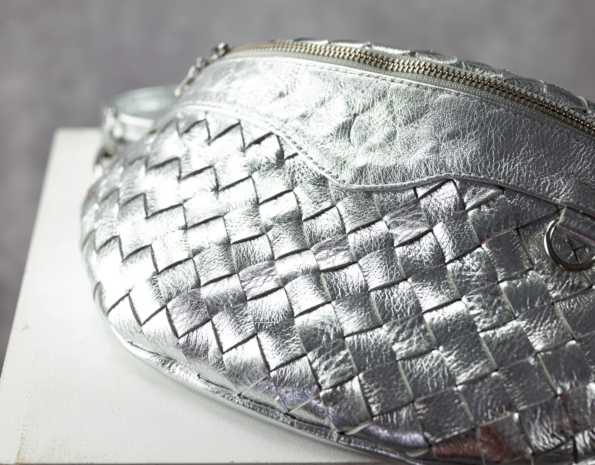 Silver woven handbag on a white surface with a gray background