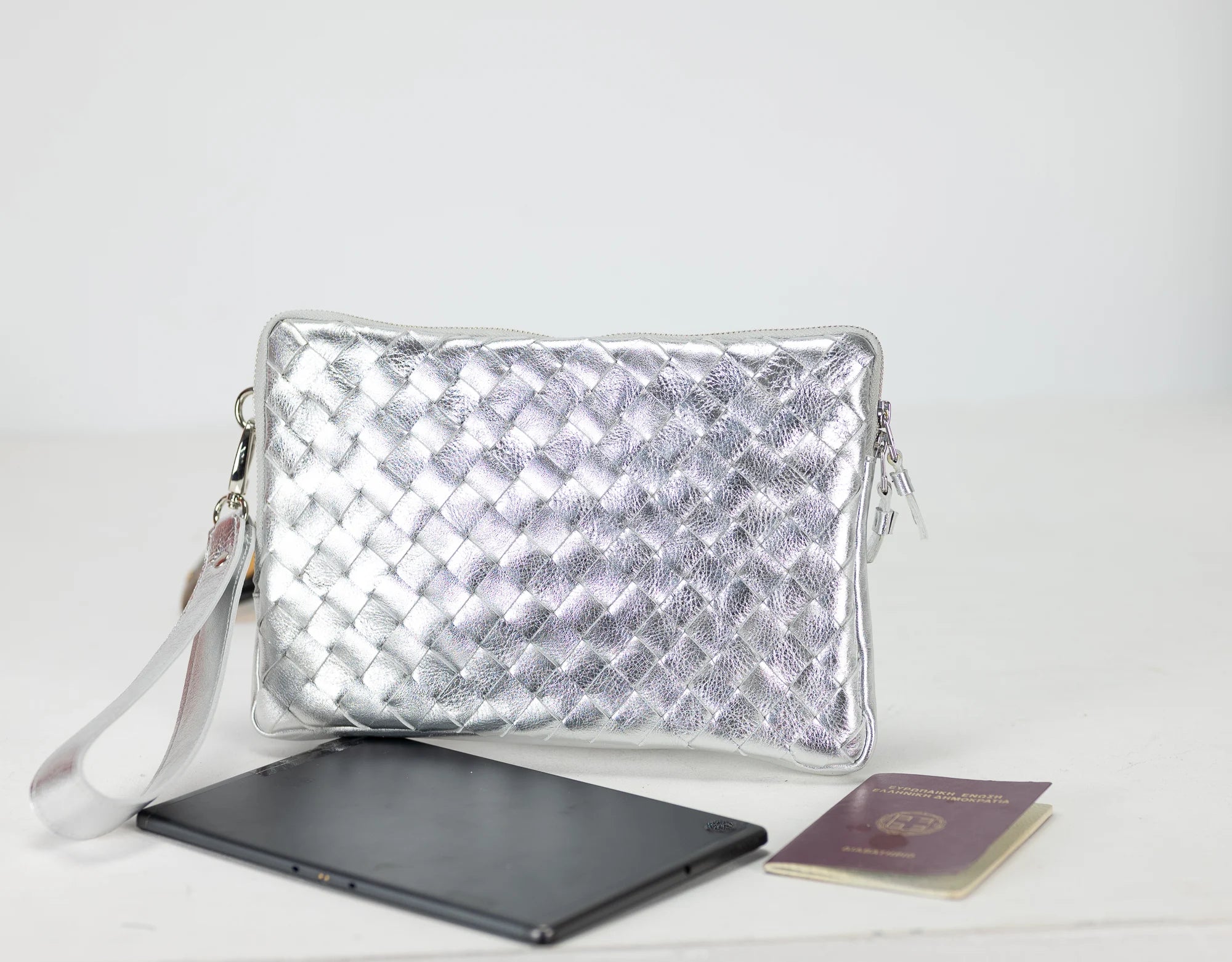 Silver woven clutch bag with a laptop and passport on a white background