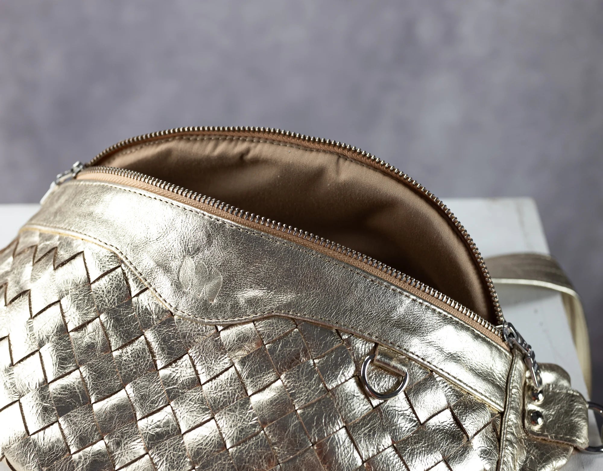 yellow gold woven handbag with a zipper on a gray background