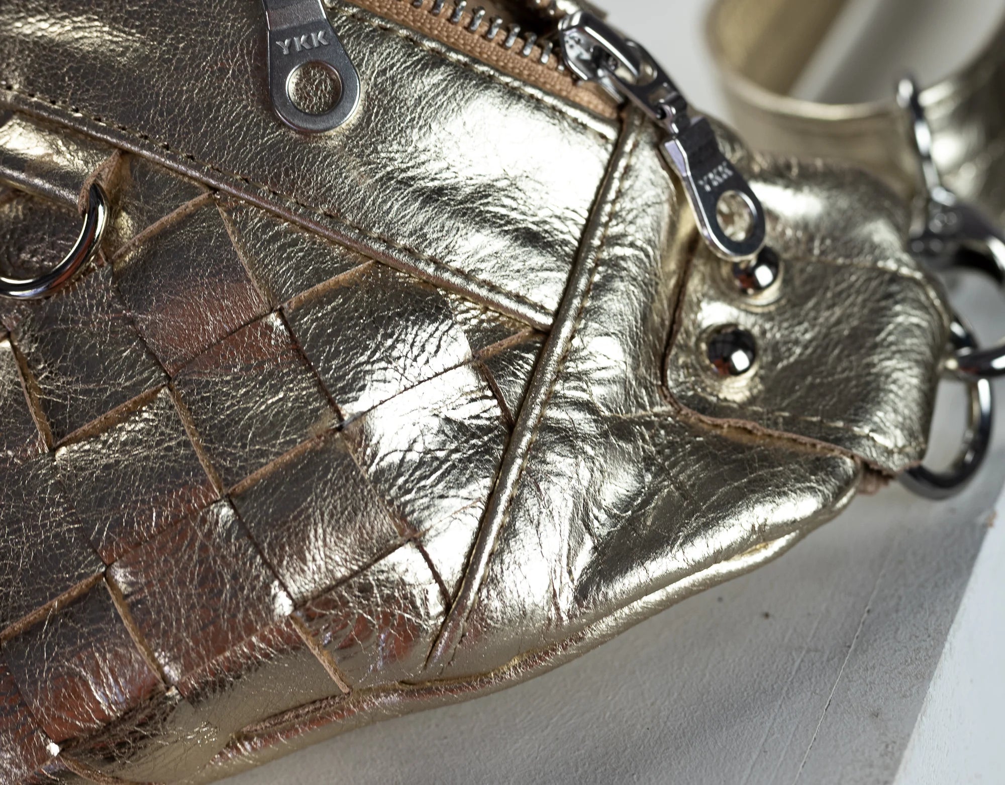 Close-up of a gold woven handbag on a white surface