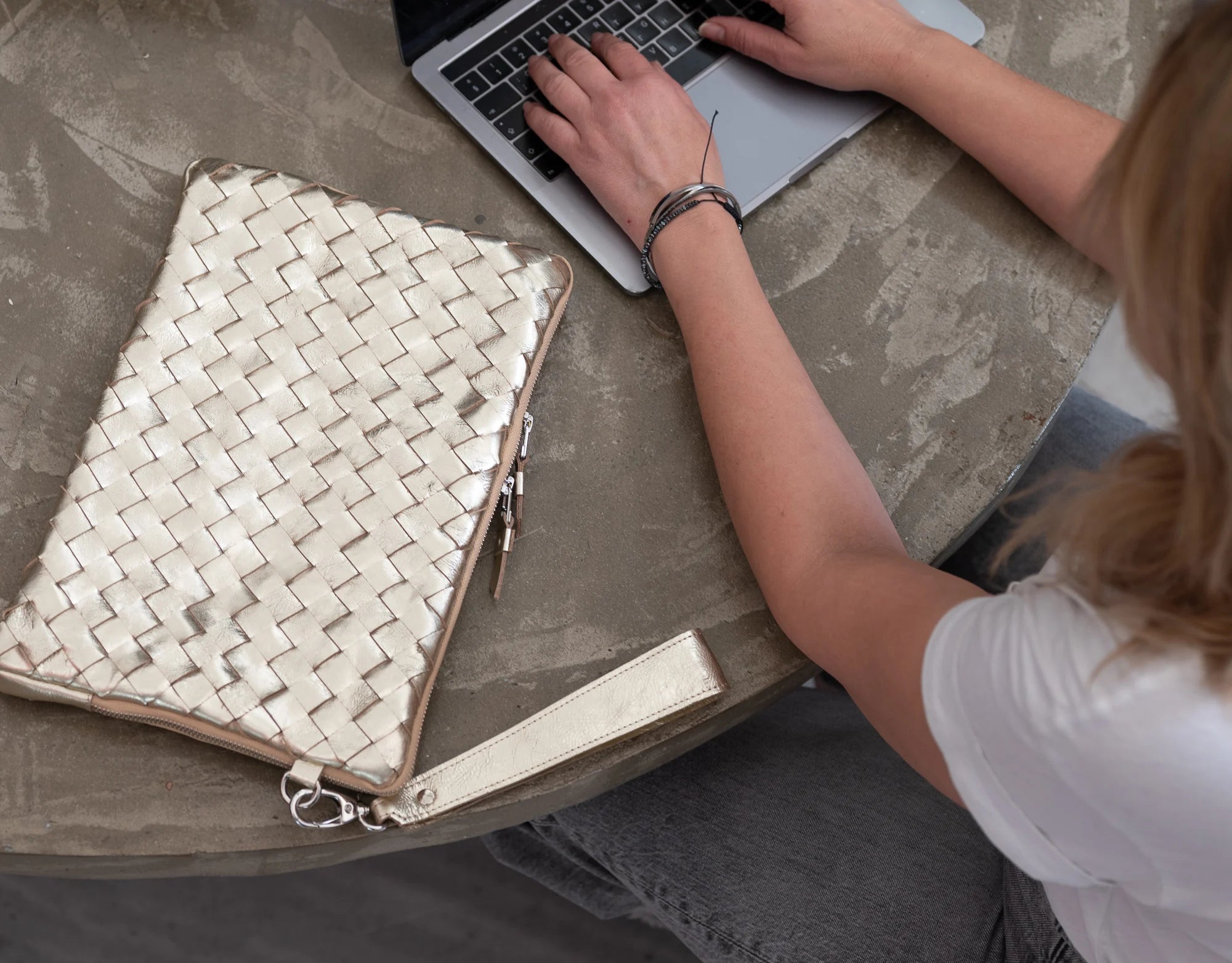 Person using a laptop with a woven clutch on a table