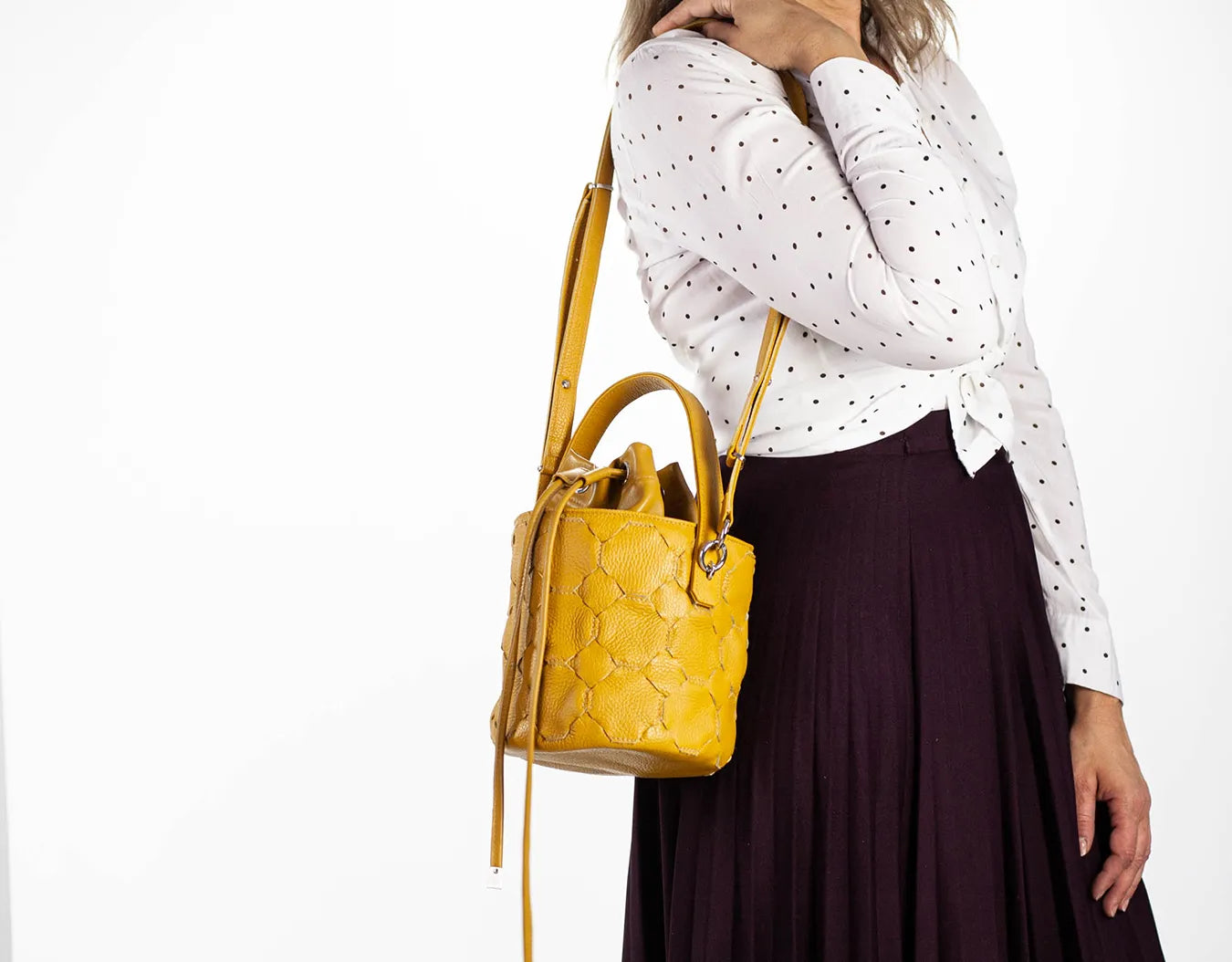 Woman holding a yellow handbag wearing a white polka dot shirt and dark skirt on a white background