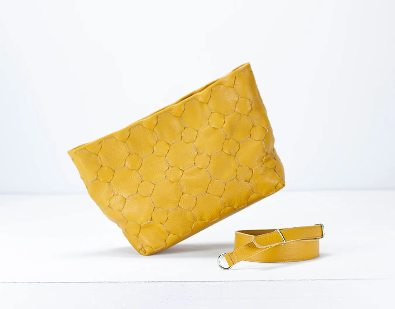 Yellow woven clutch bag with matching strap on a light gray background