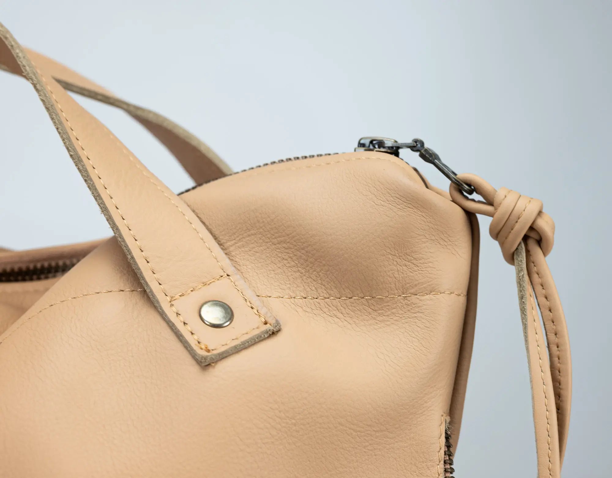 Beige leather handbag with a strap on a light gray background