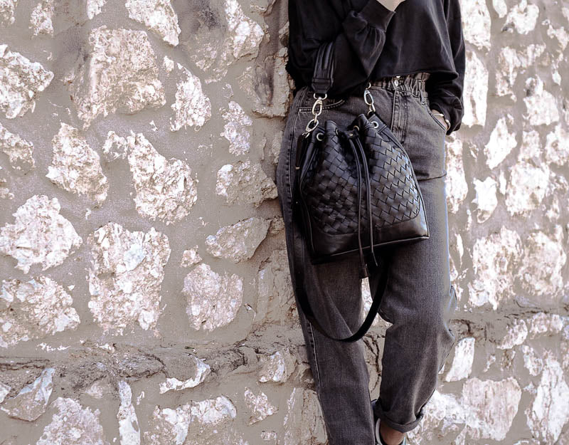 Person holding a textured black handbag against a stone wall