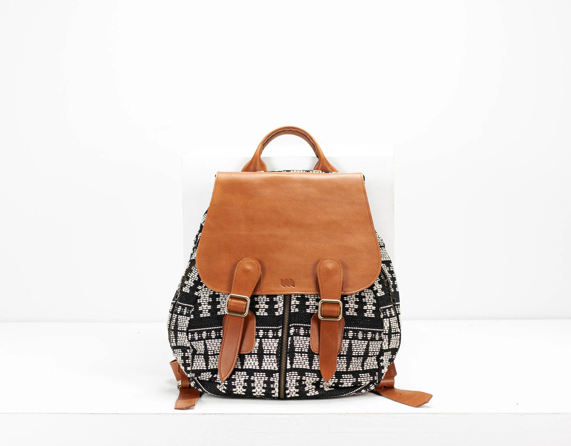 Backpack with black and white pattern and brown leather straps on a white background