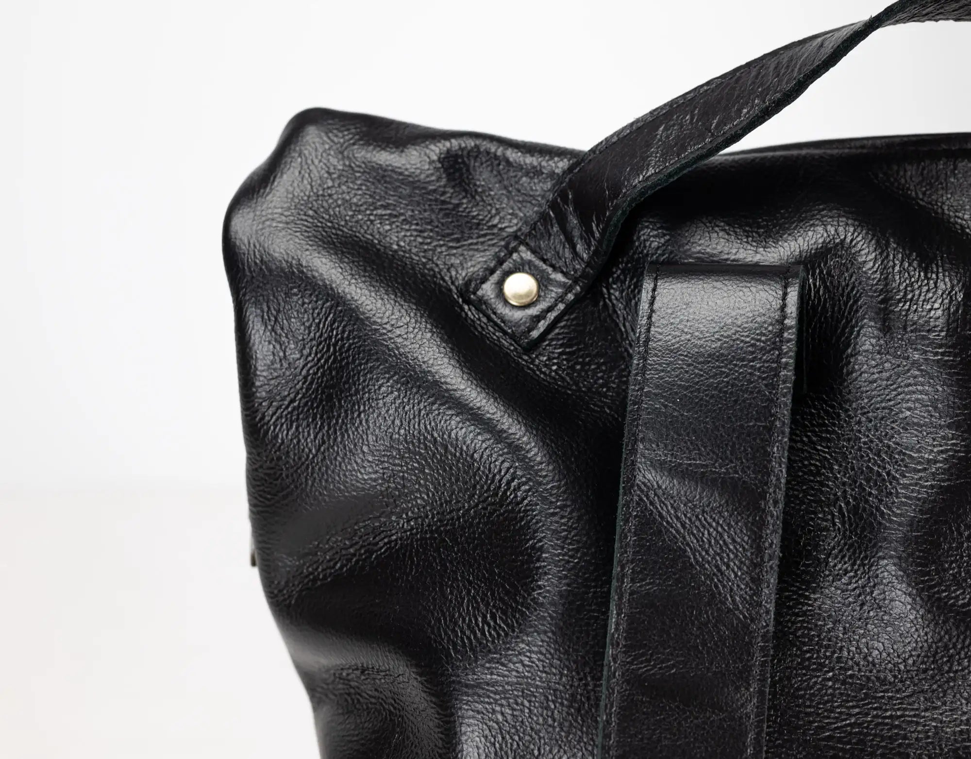 Close-up of a black leather bag with a strap on a white background