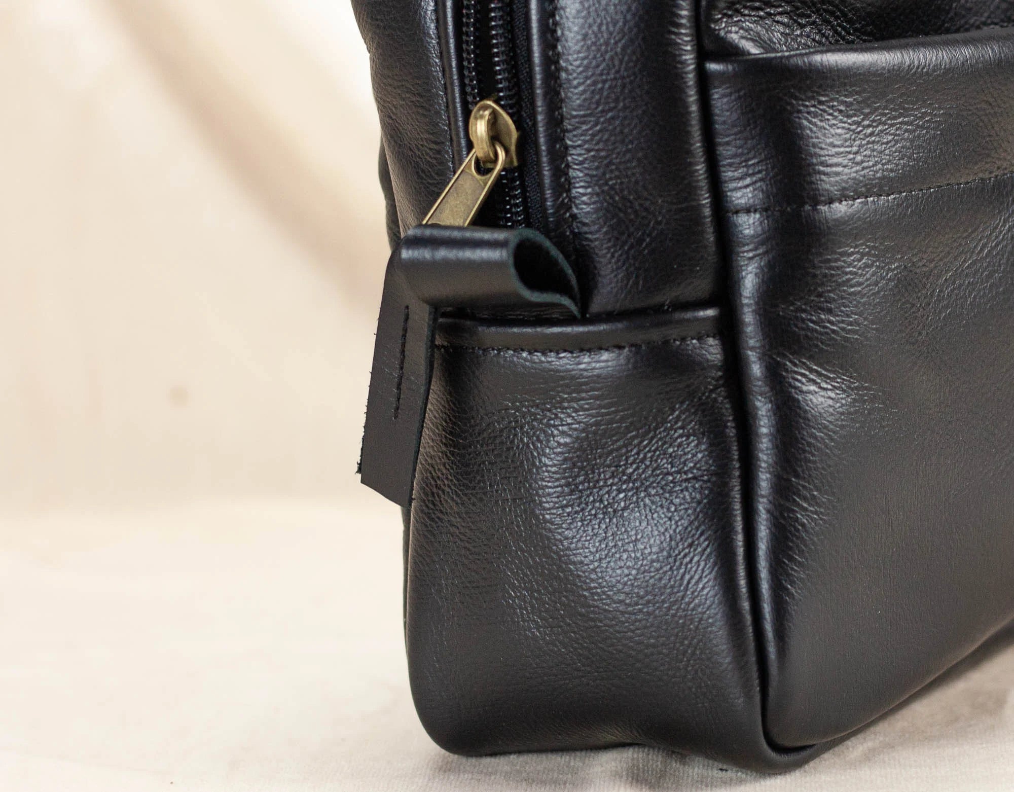 Close-up of a black leather bag with a gold zipper on a beige background