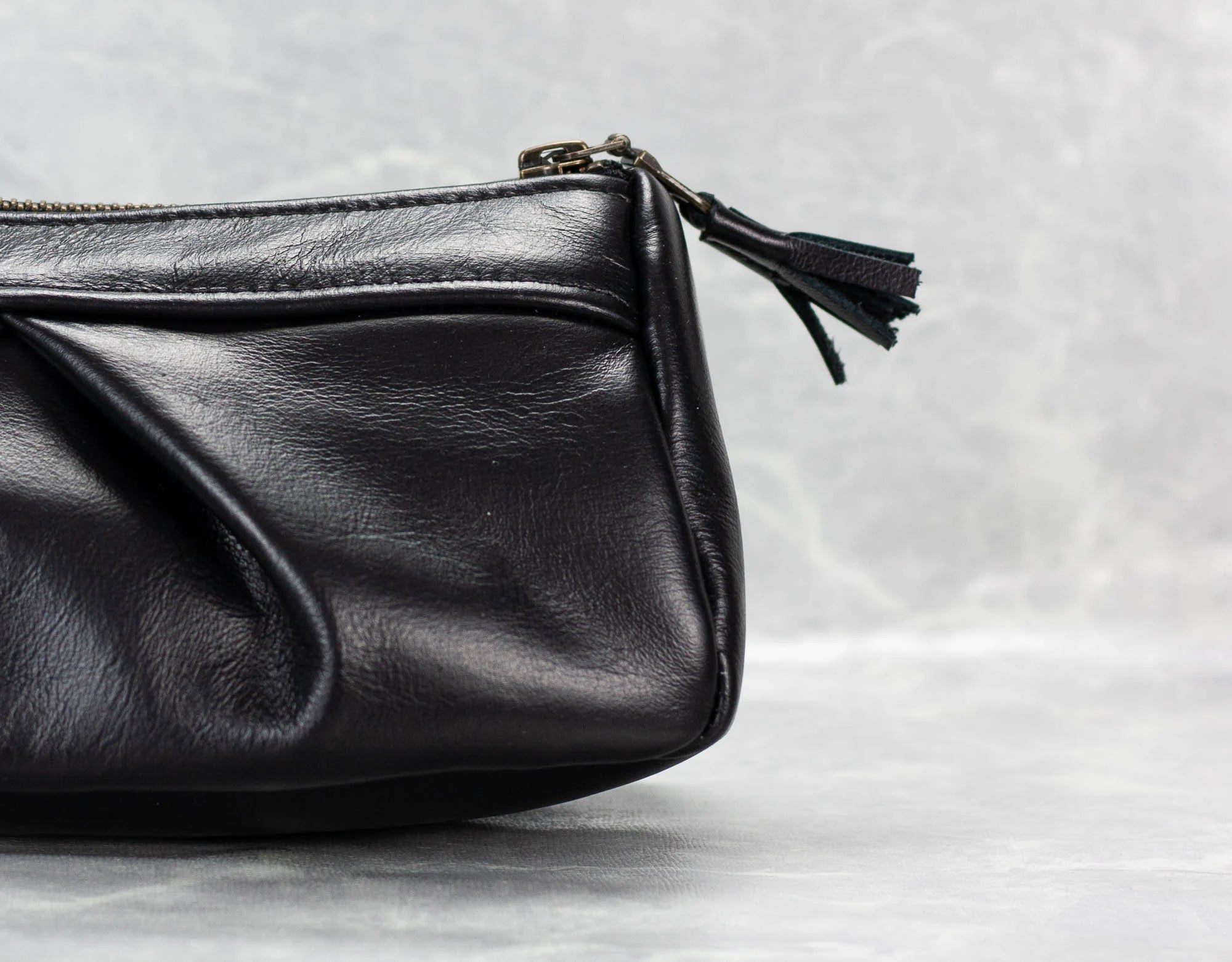 Black leather clutch bag with a tassel on a light gray background