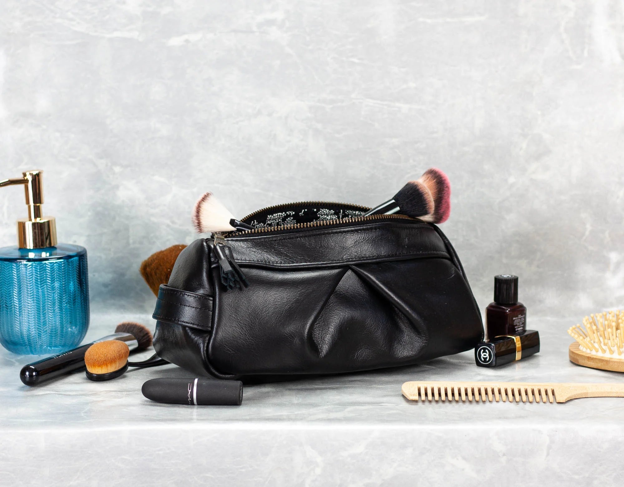 Black leather toiletry bag with makeup items on a gray surface