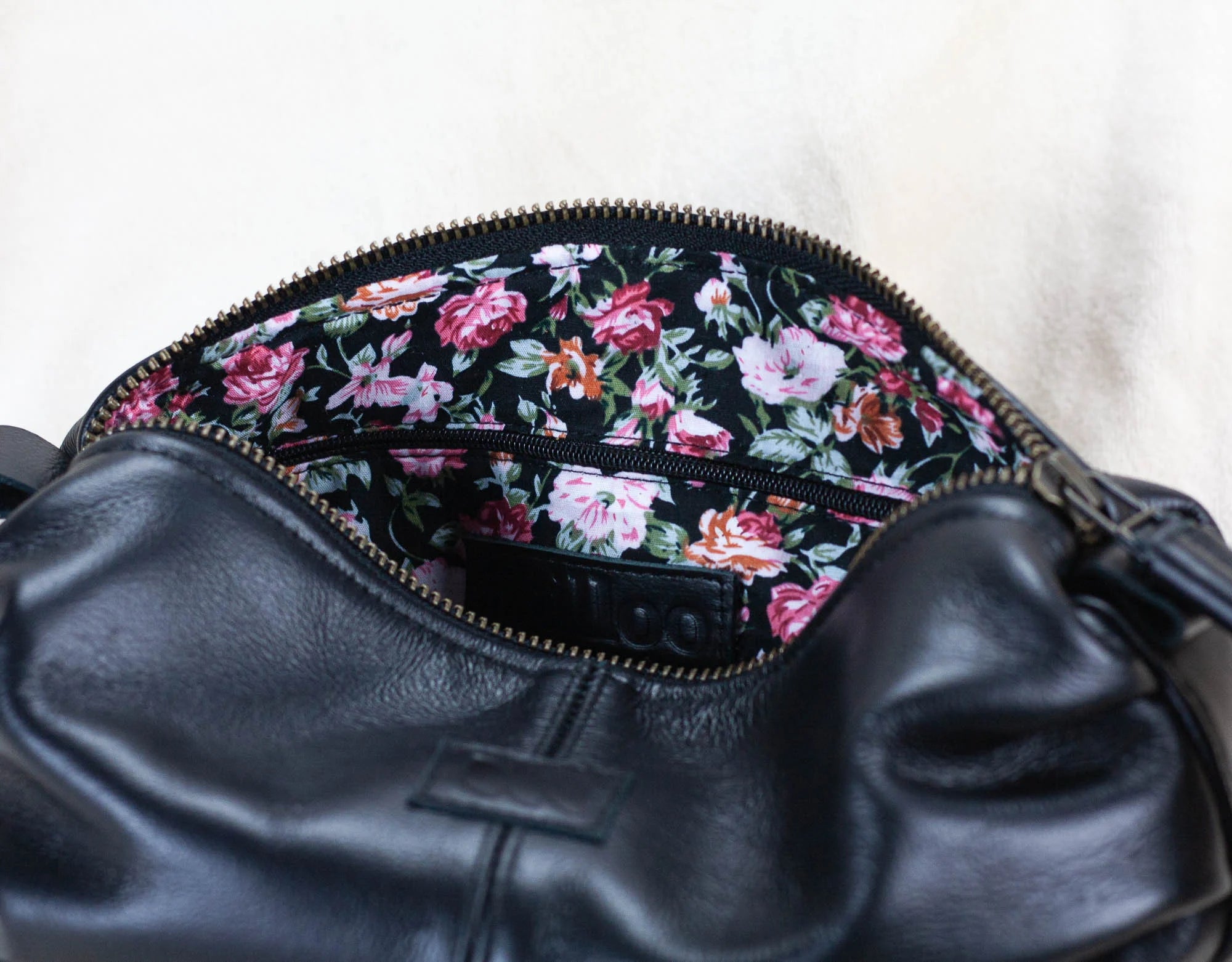 Black leather bag with floral patterned zipper on a white background