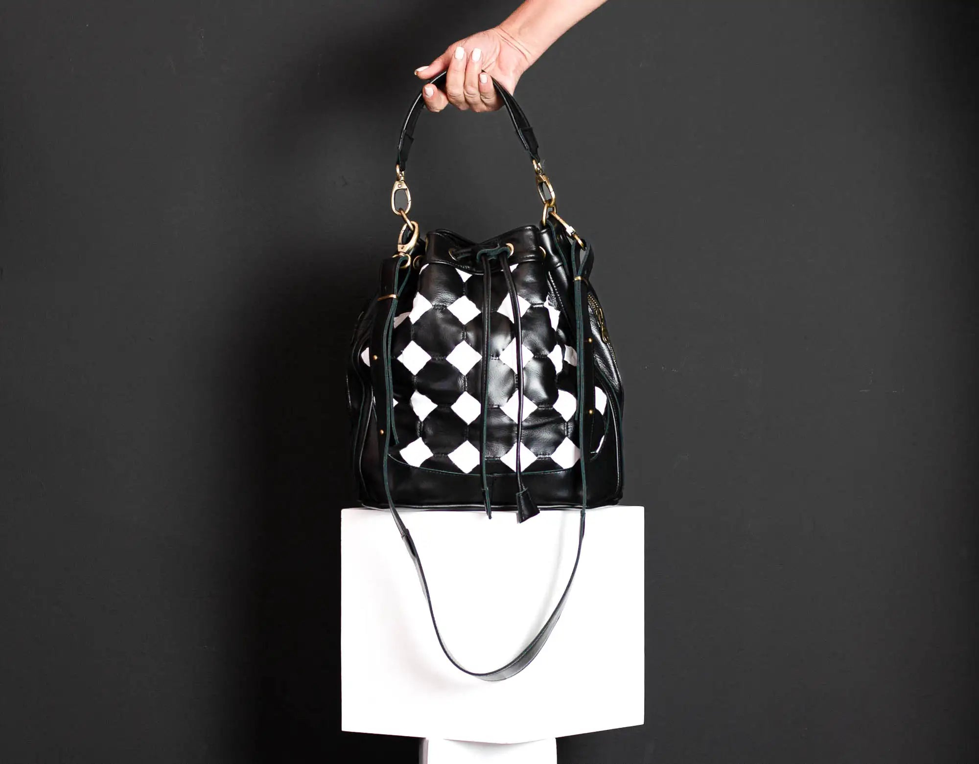 Black and white checkered handbag held by a person against a dark background