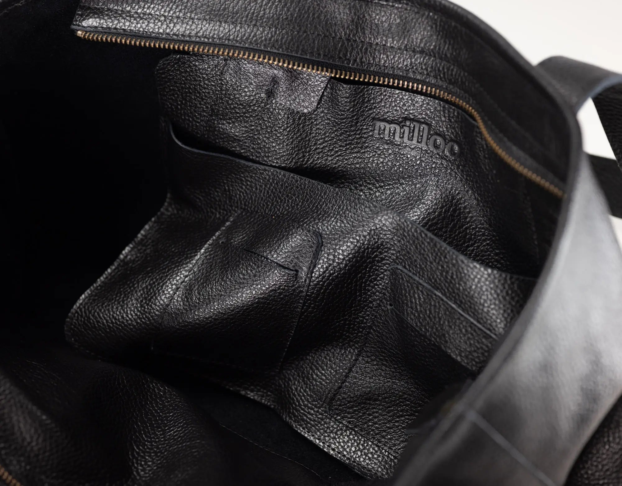 Close-up of the interior of a black pebbled leather bag, showing a zippered compartment and the embossed brand name &
