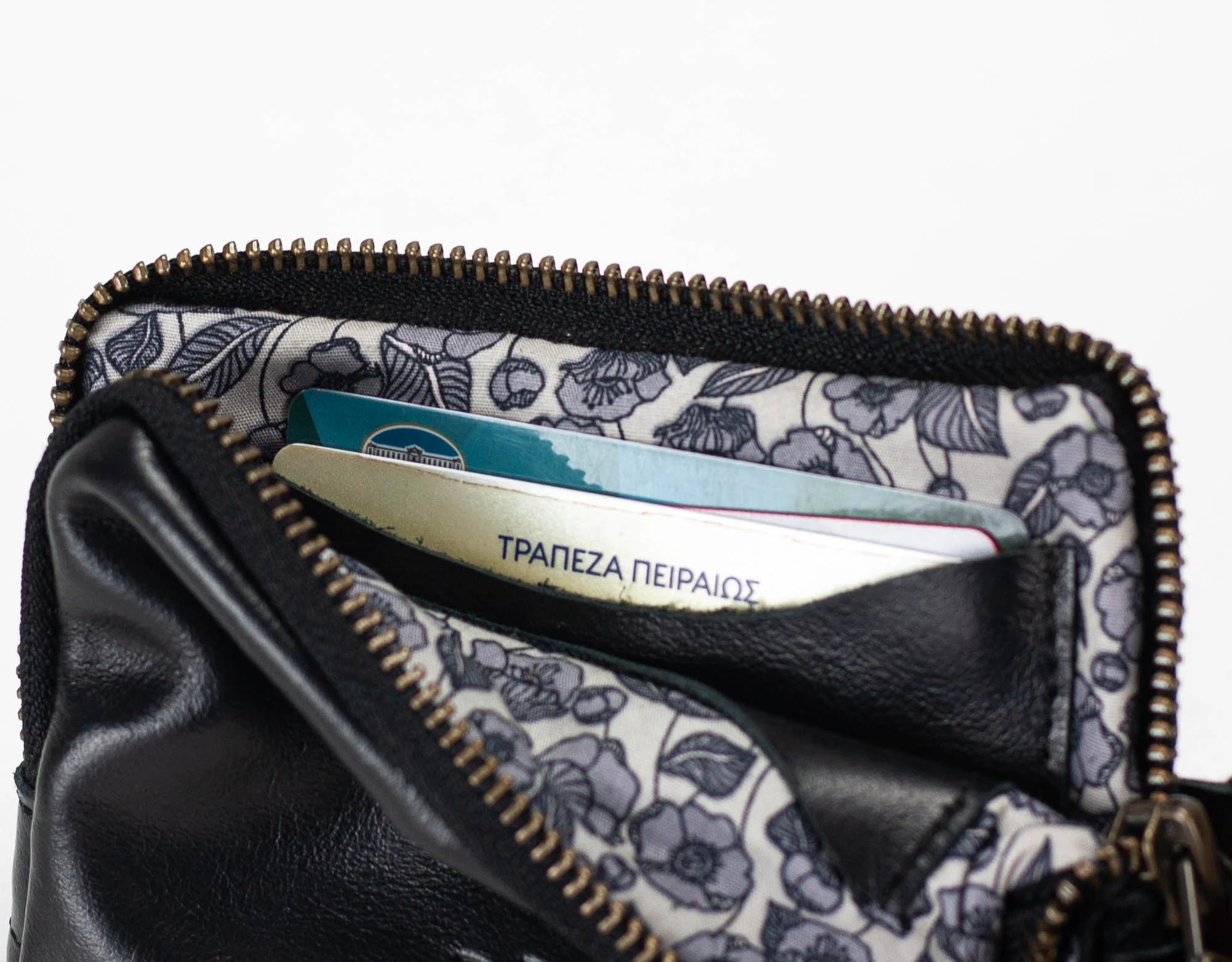 Black leather wallet with floral lining holding a bank card on a white background